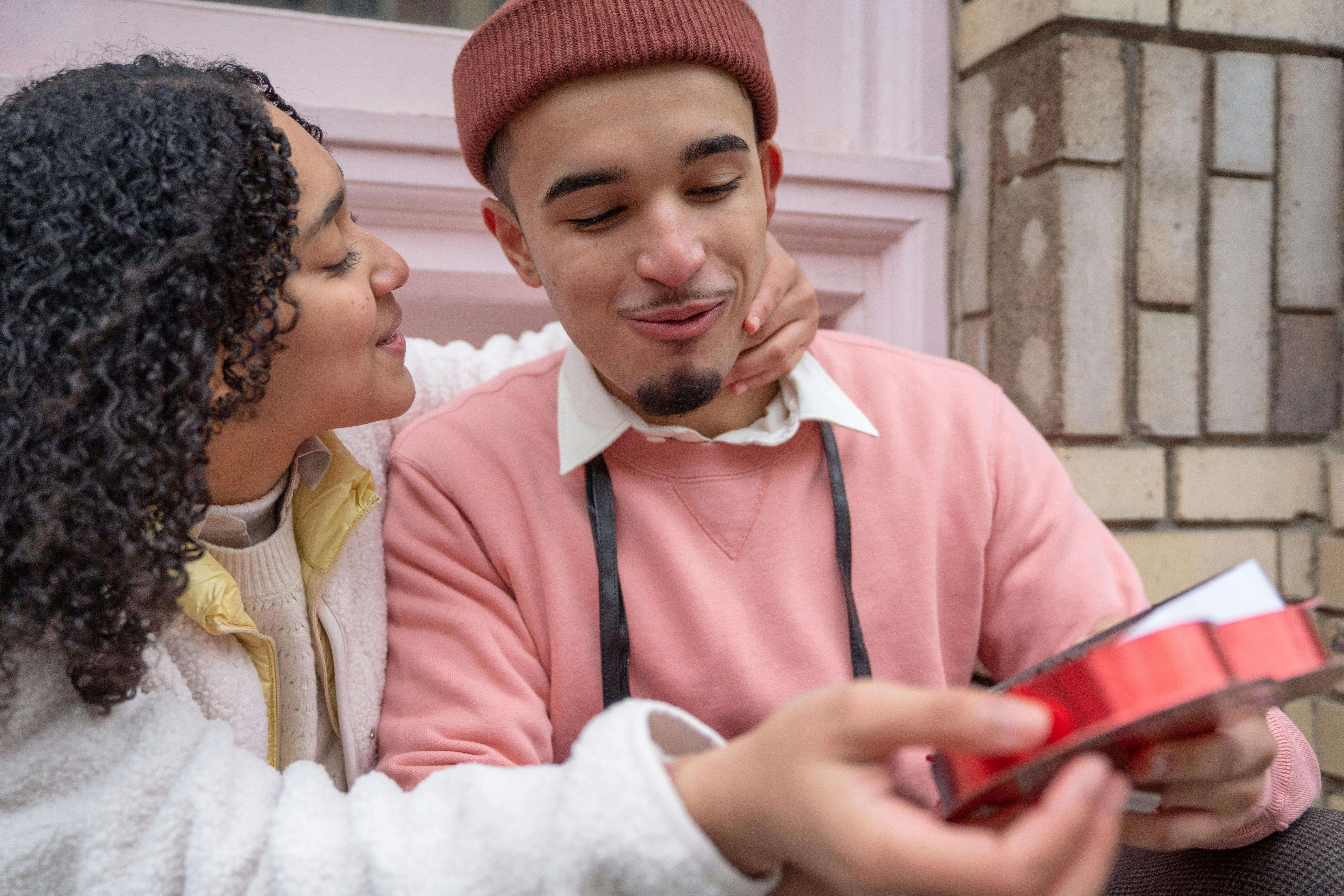 Crop happy young Hispanic female smiling and embracing boyfriend on street after getting heart shaped chocolate gift box on Saint Valentines Day