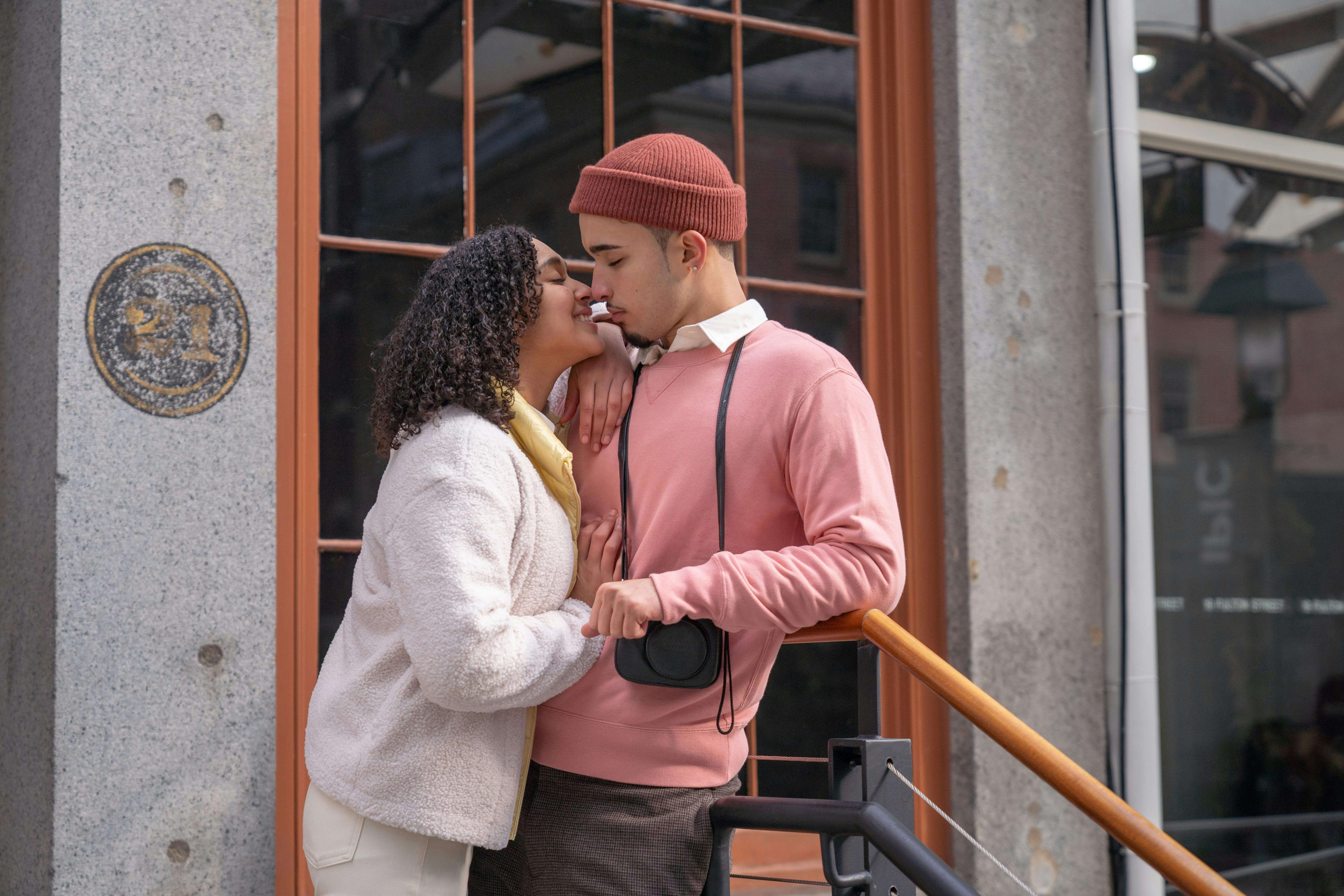 A couple shares a tender moment outdoors in a city environment.