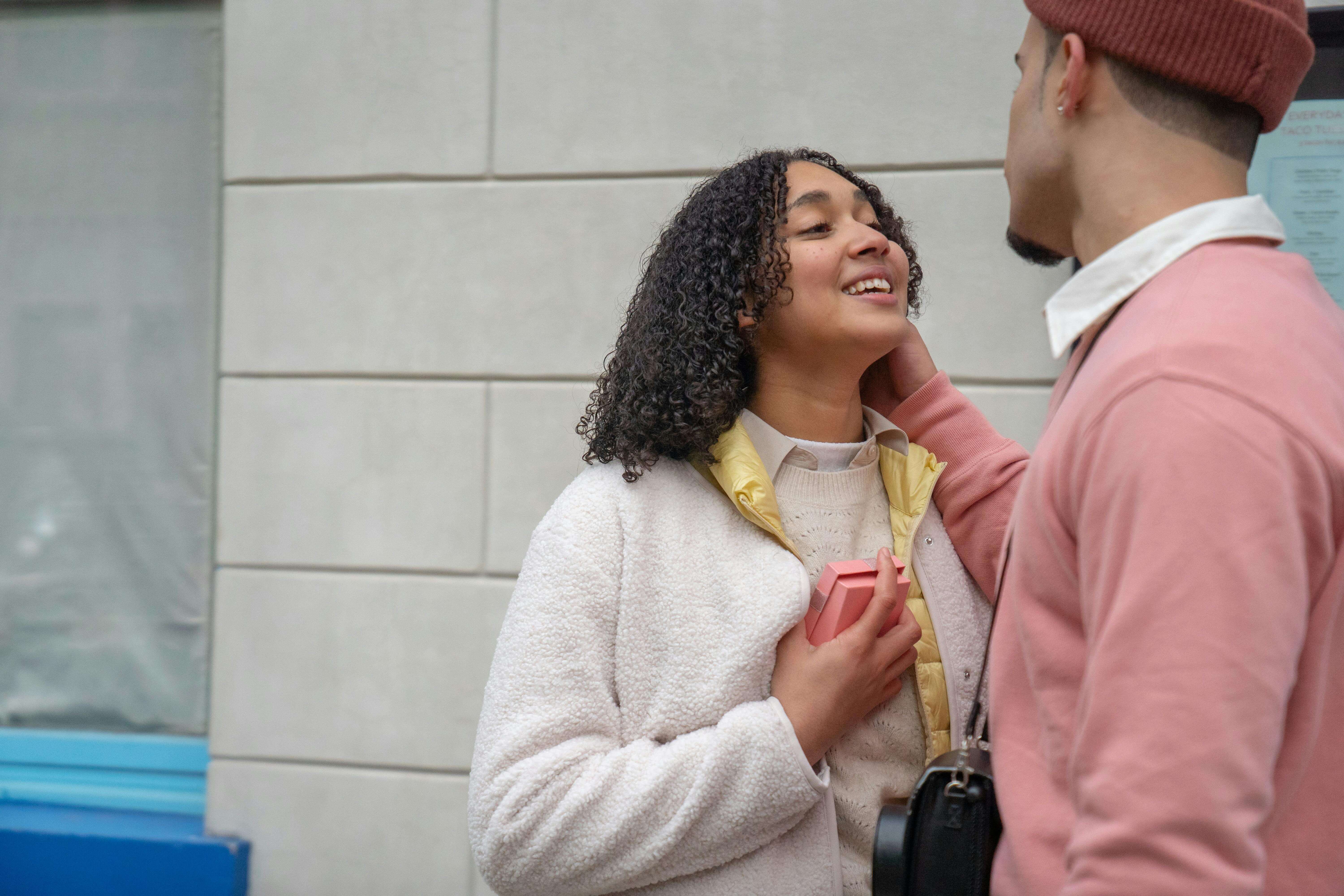 A joyful couple sharing a moment of affection outdoors, holding a gift box, embodying love and romance.