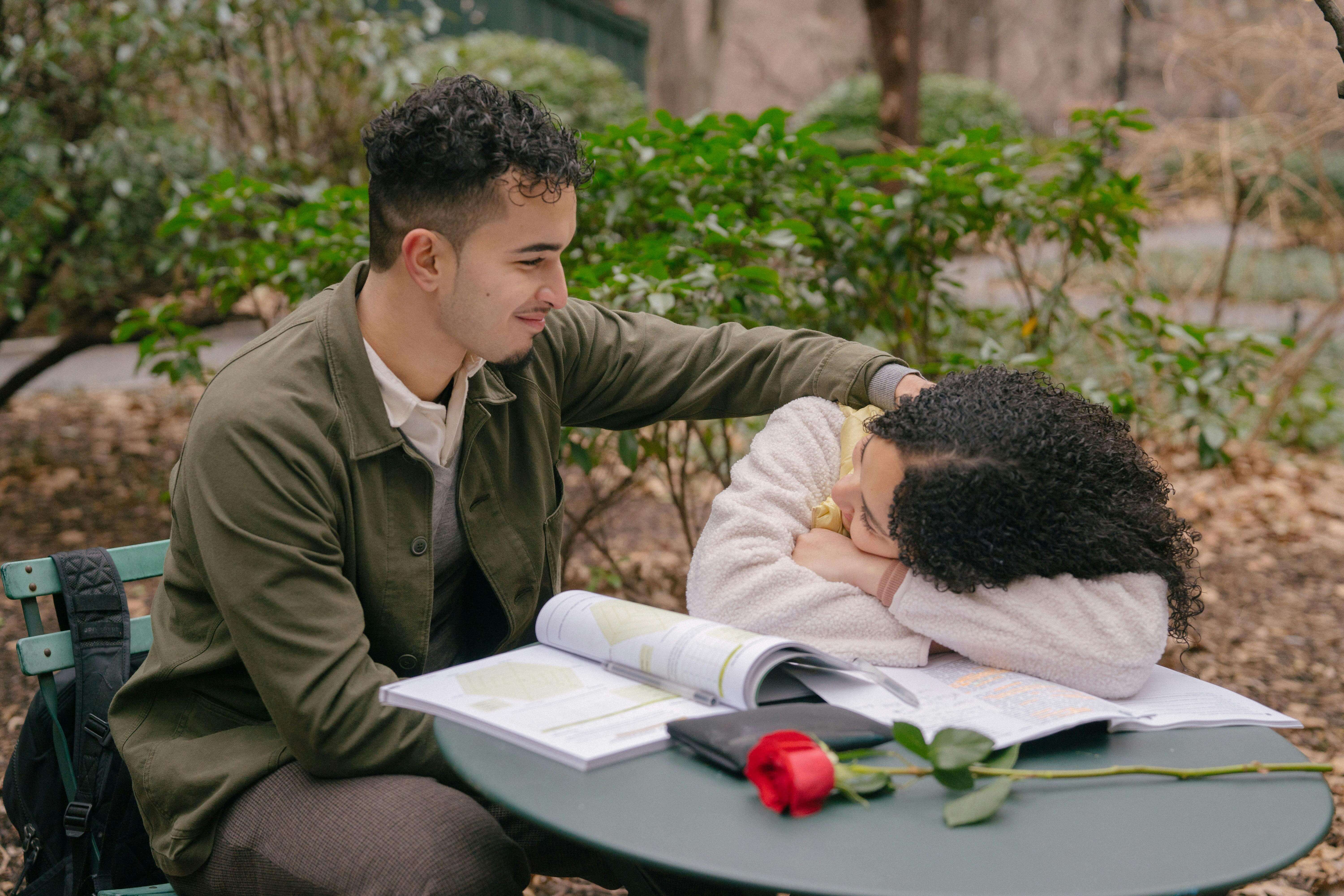 A young couple enjoying a tender moment while studying together in a park.
