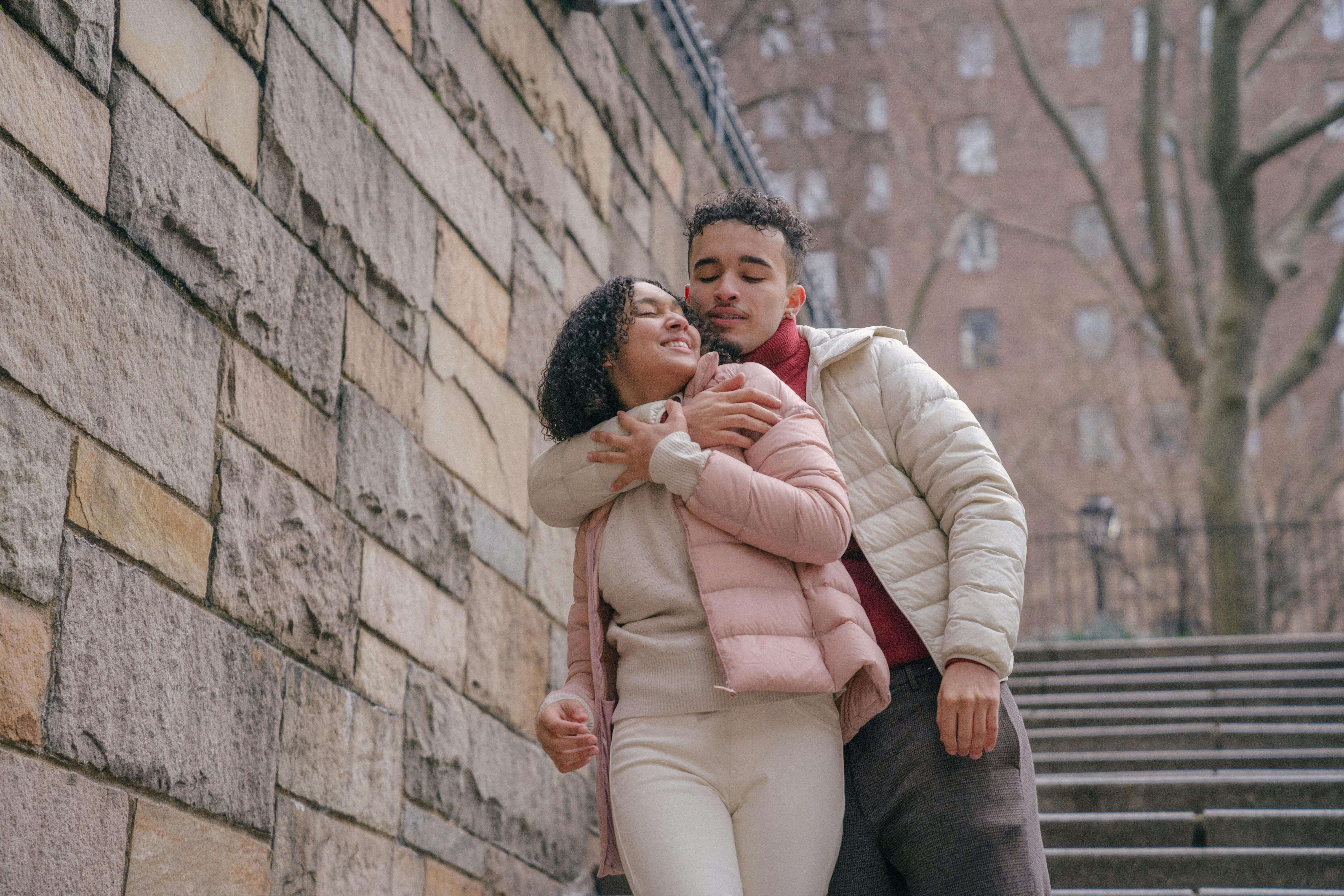 Happy couple embracing affectionately on urban steps in warm winter clothes.