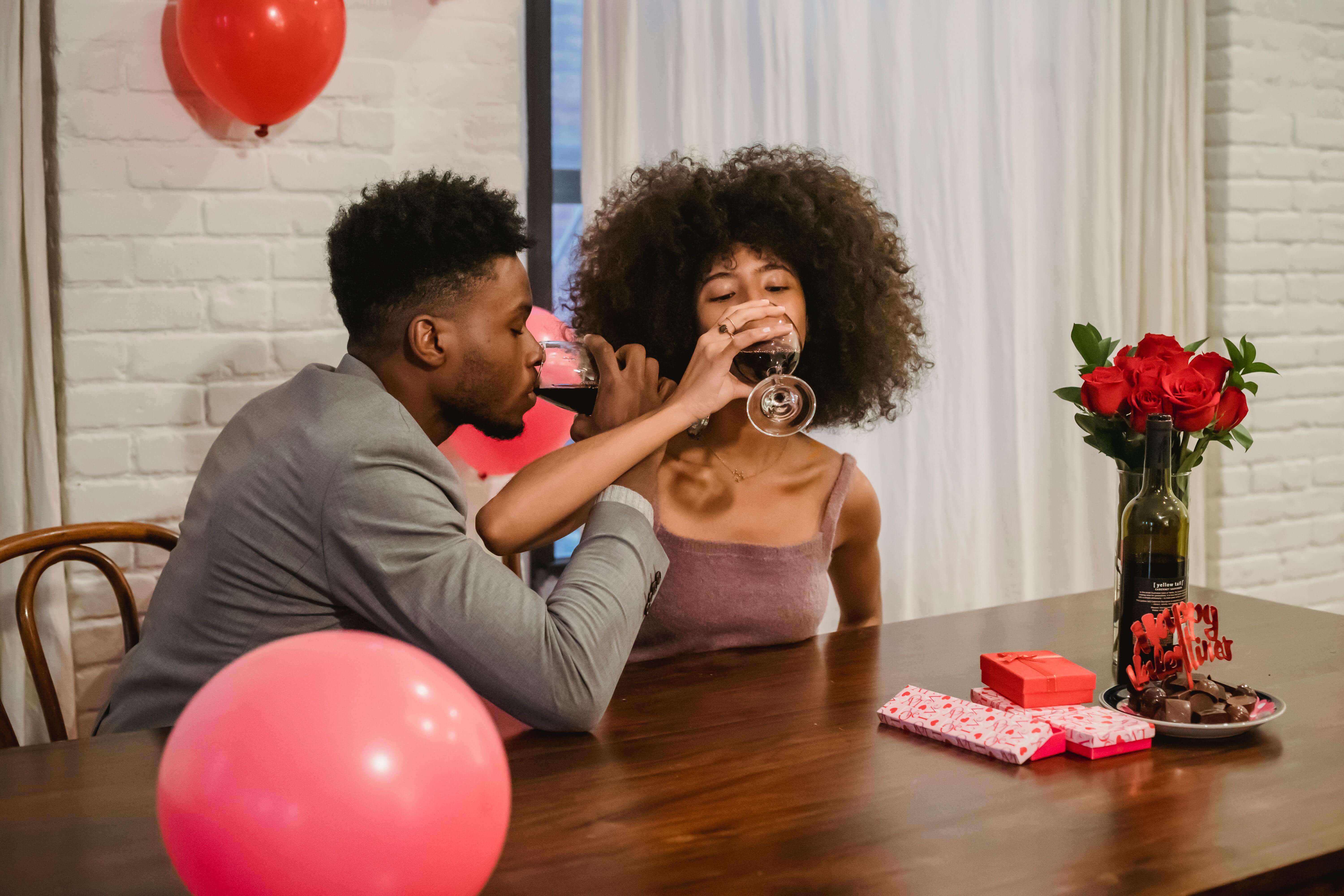 Couple enjoying a romantic Valentine's Day celebration indoors with wine and gifts.