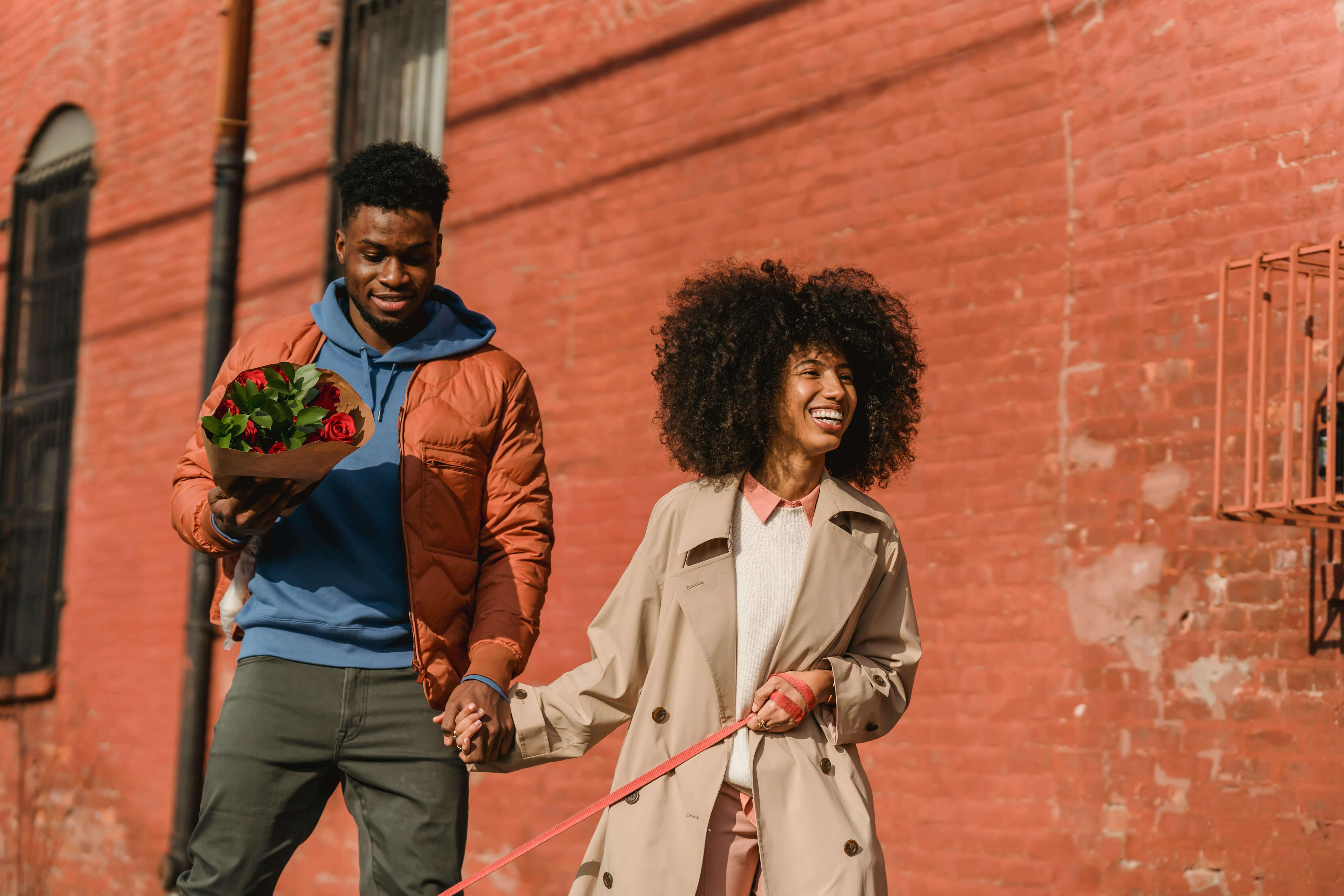 Smiling couple holding hands and flowers during a sunny walk, enjoying each other's company.