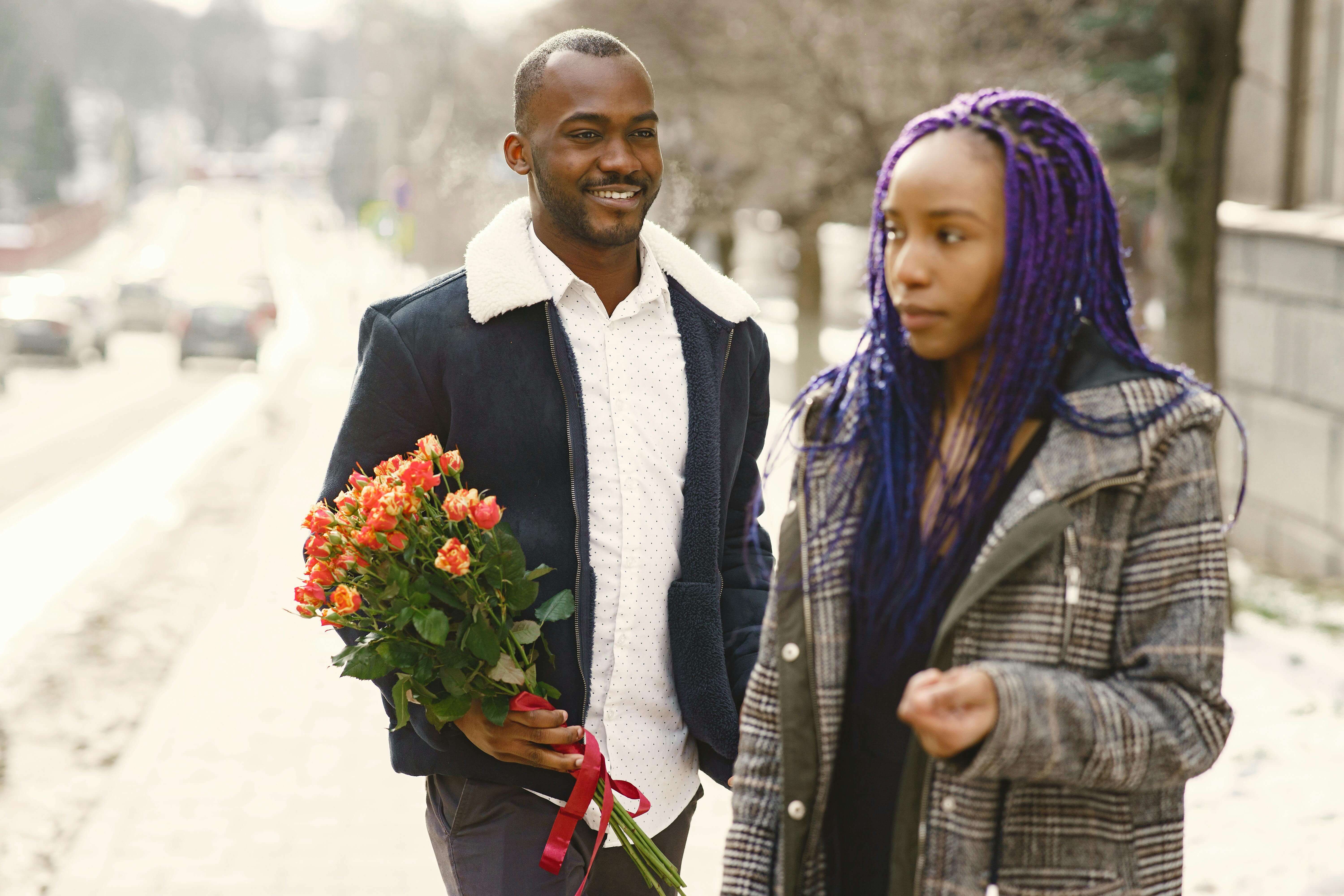 A couple strolling outdoors with a bouquet of flowers, sharing a moment of love.