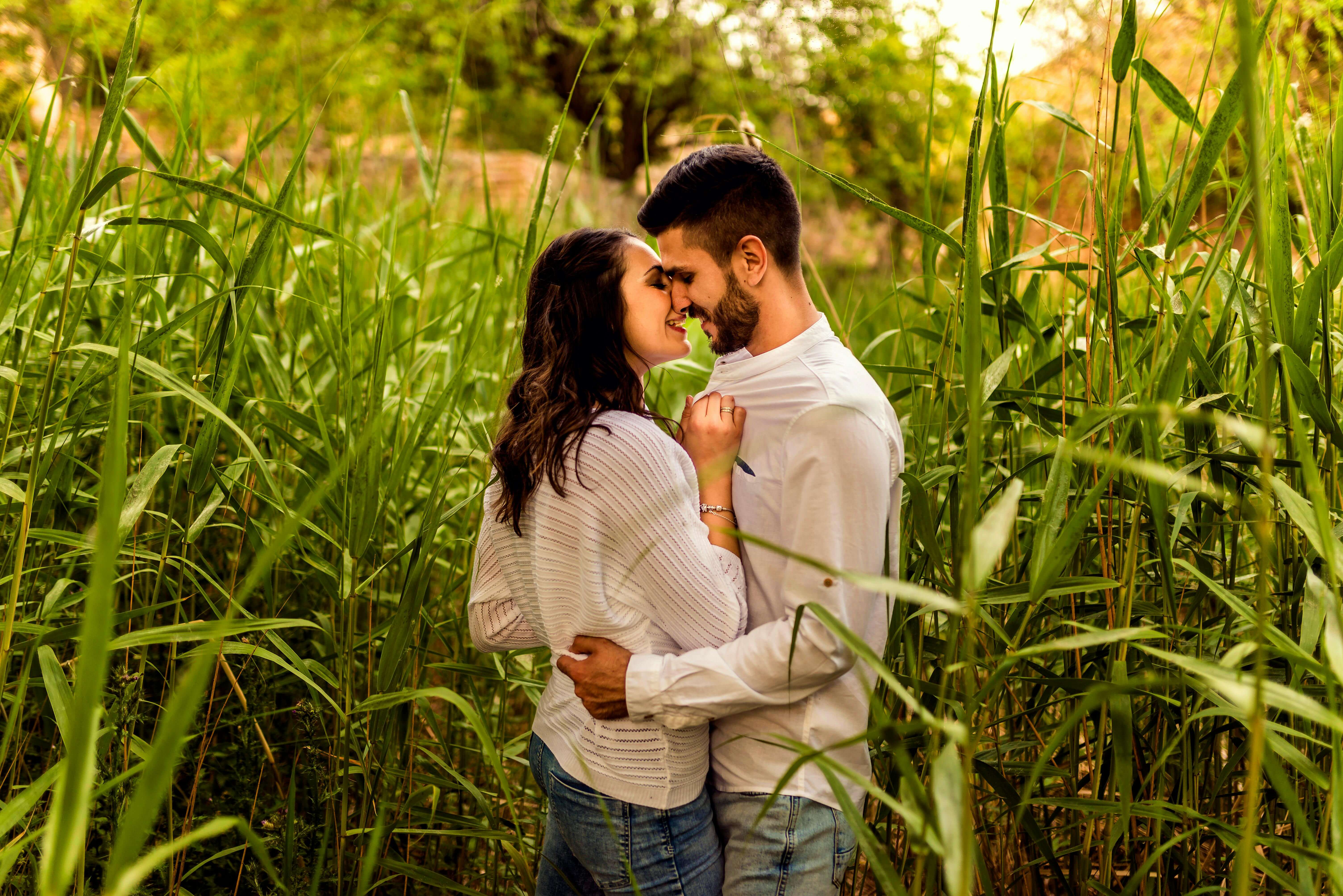 A loving couple shares a tender moment surrounded by lush greenery in a field during summer.