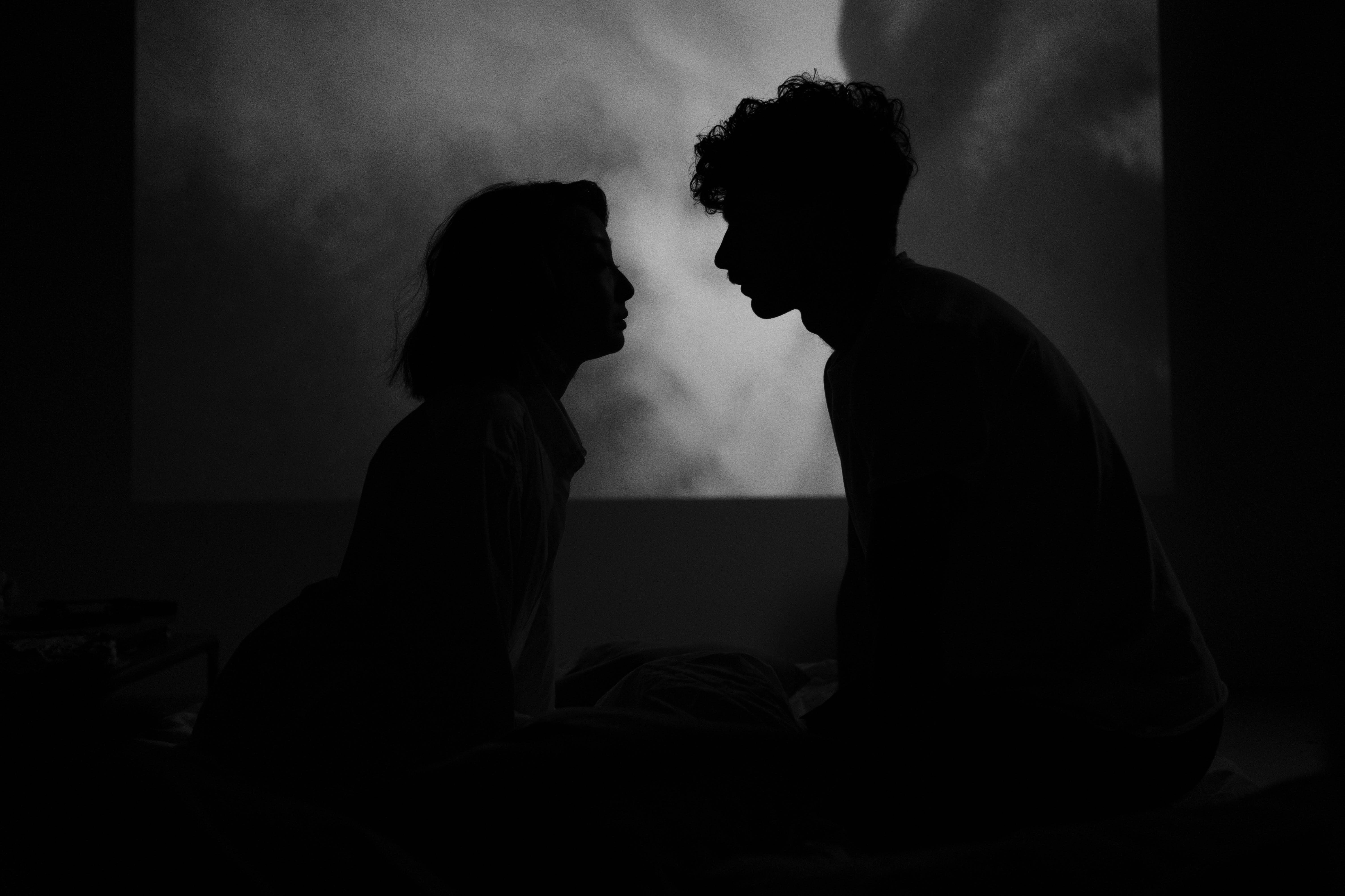A romantic silhouette of a couple facing each other captured in a dark, black and white setting indoors.