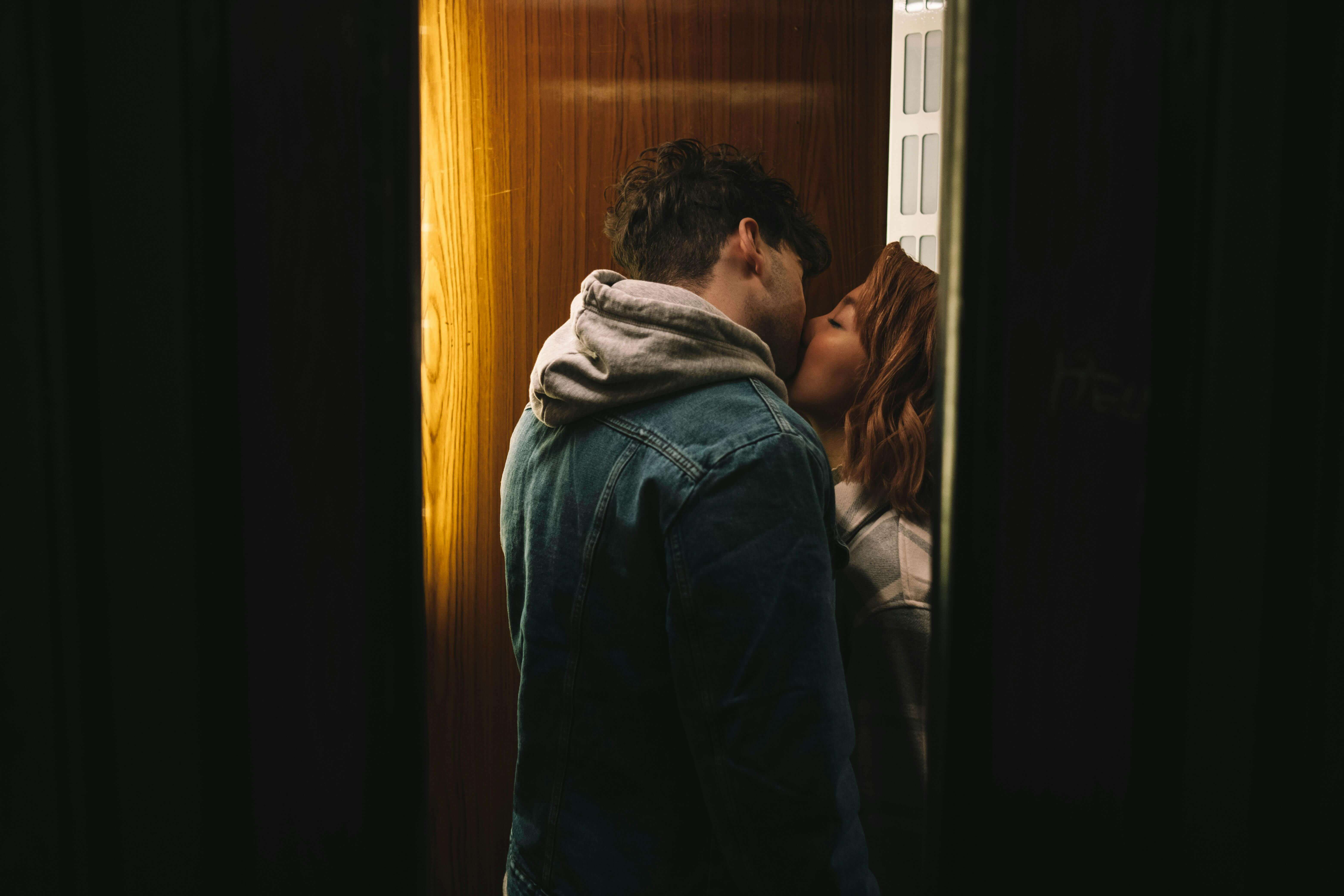 A couple shares an intimate kiss in a cozy elevator setting, conveying love and affection.
