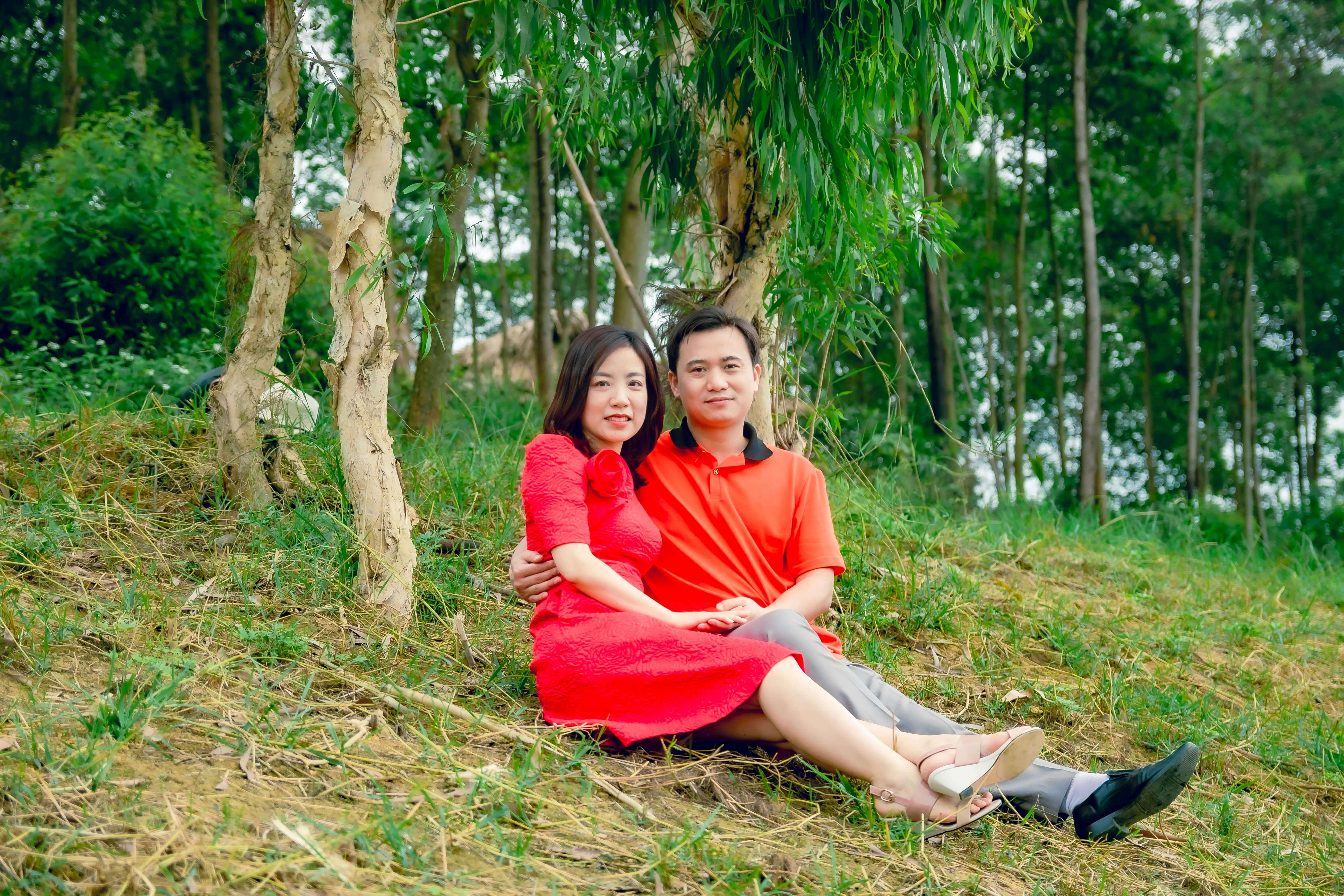 Asian couple enjoying a peaceful moment together on a grassy hill surrounded by trees.