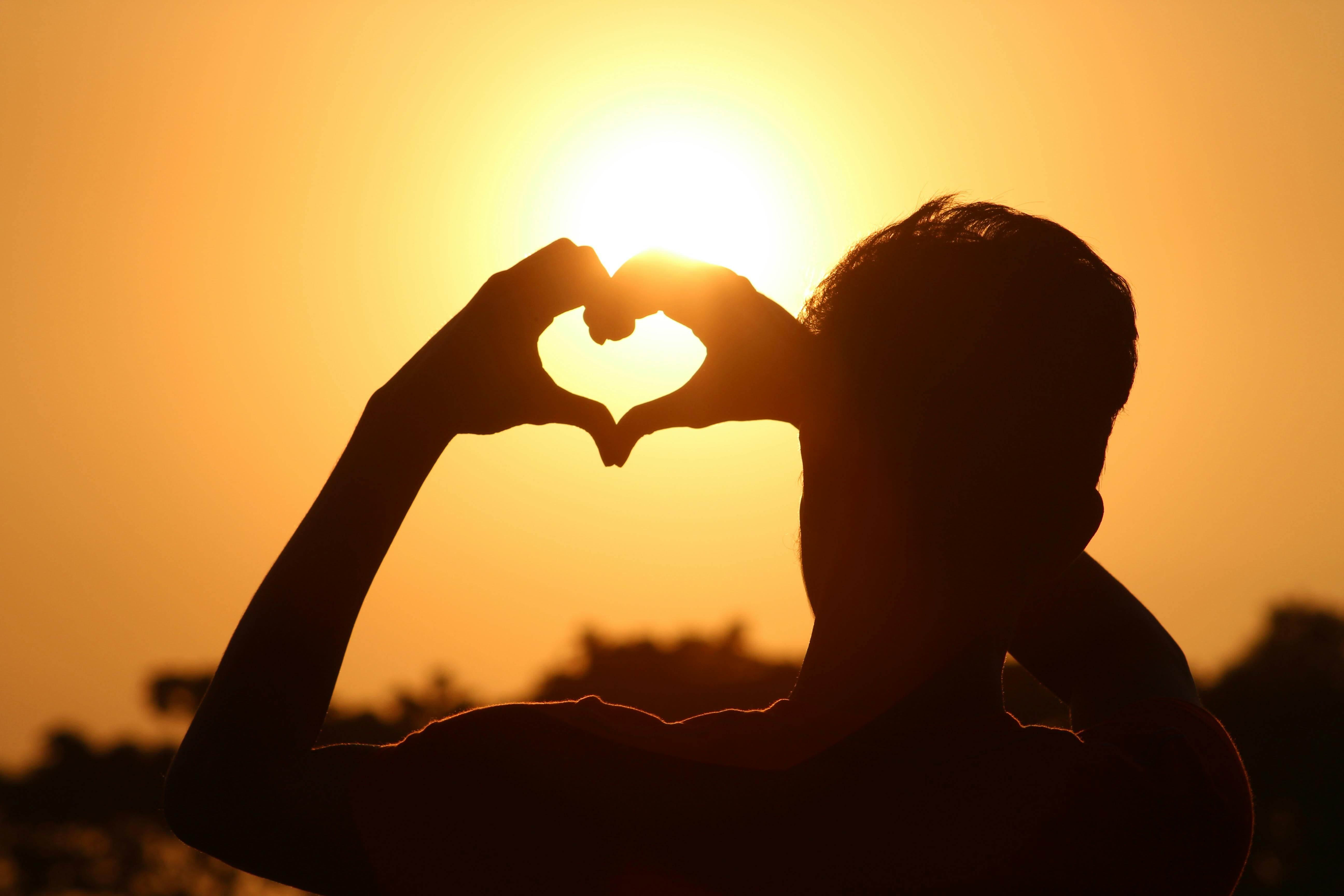 A silhouette of hands forming a heart shape against a vibrant sunset in Bangladesh.