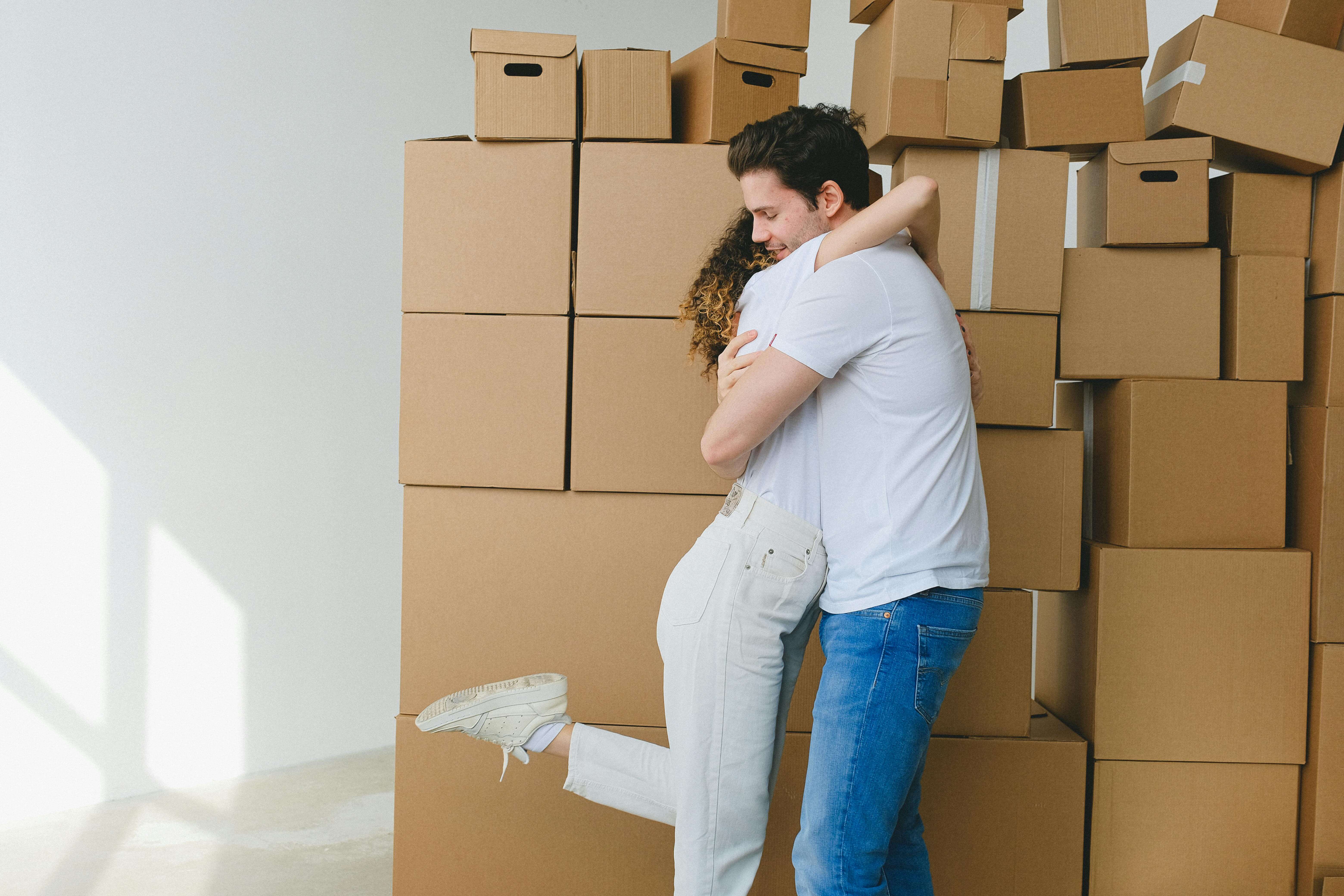 A cheerful couple hugs surrounded by moving boxes, celebrating their new home.