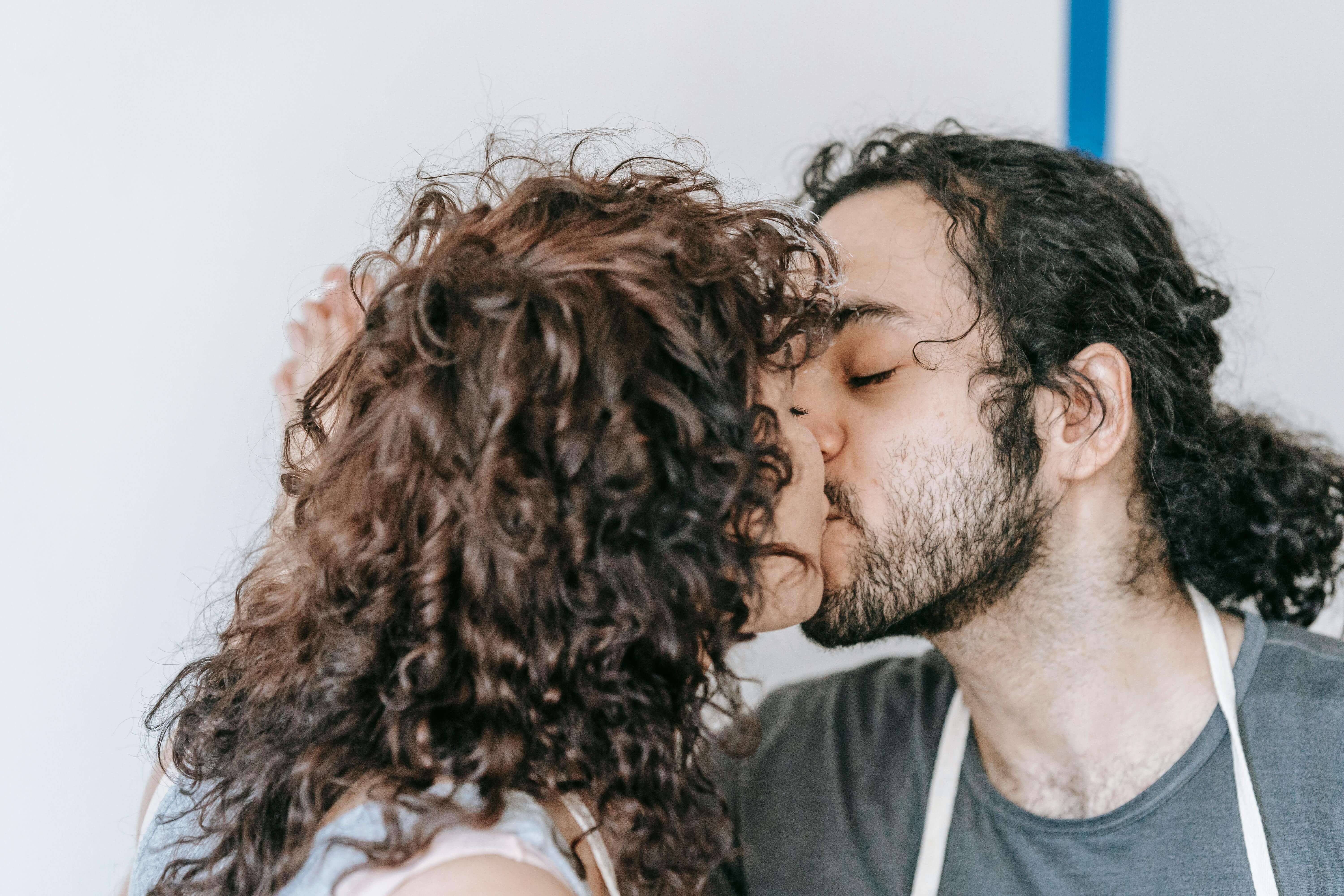 A young couple shares a tender kiss indoors, showcasing romance and love in a relaxed setting.