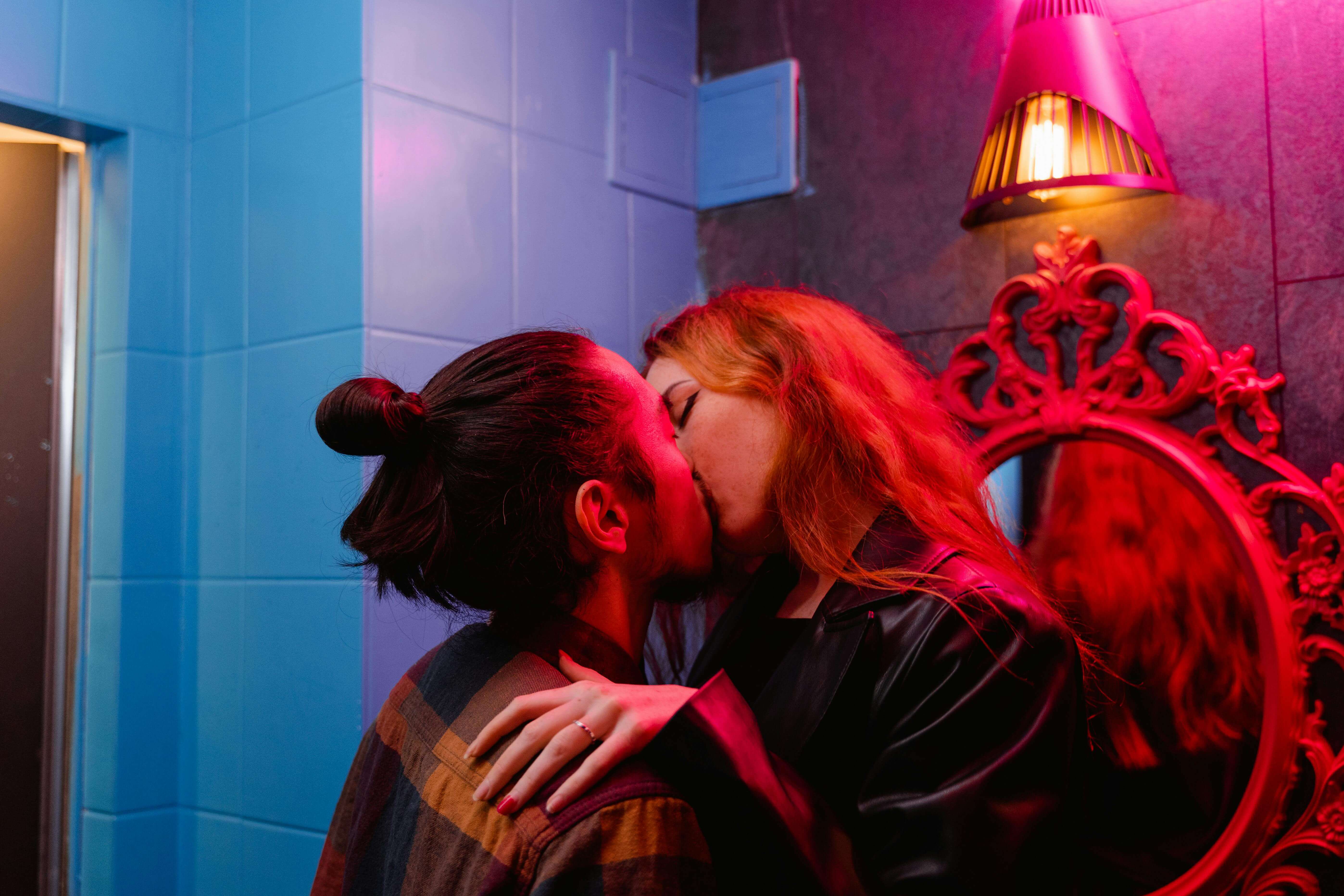 A couple shares a passionate kiss in a vibrant nightclub with colorful lighting.