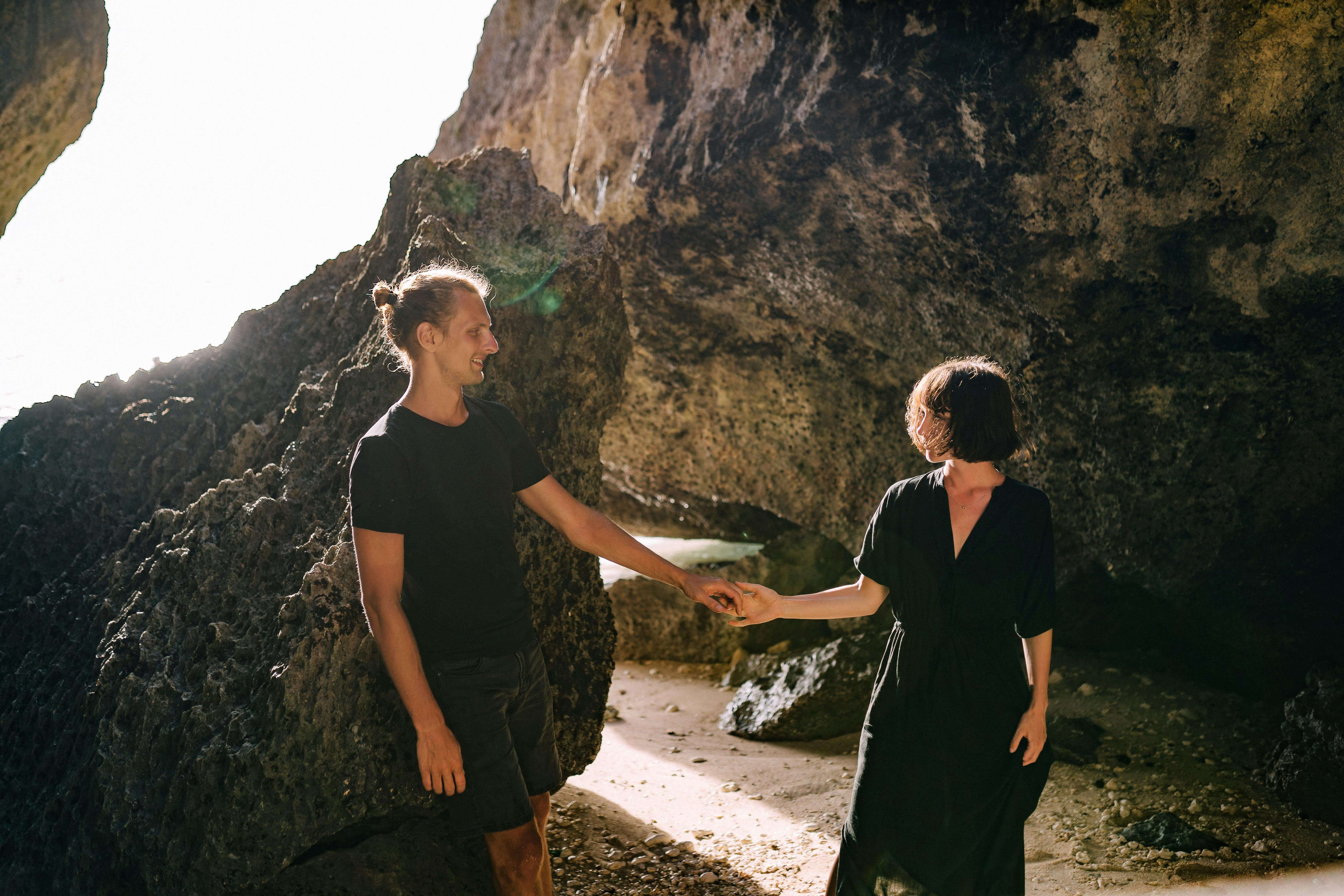 A couple holding hands in a sunlit cave, exuding romance and connection.