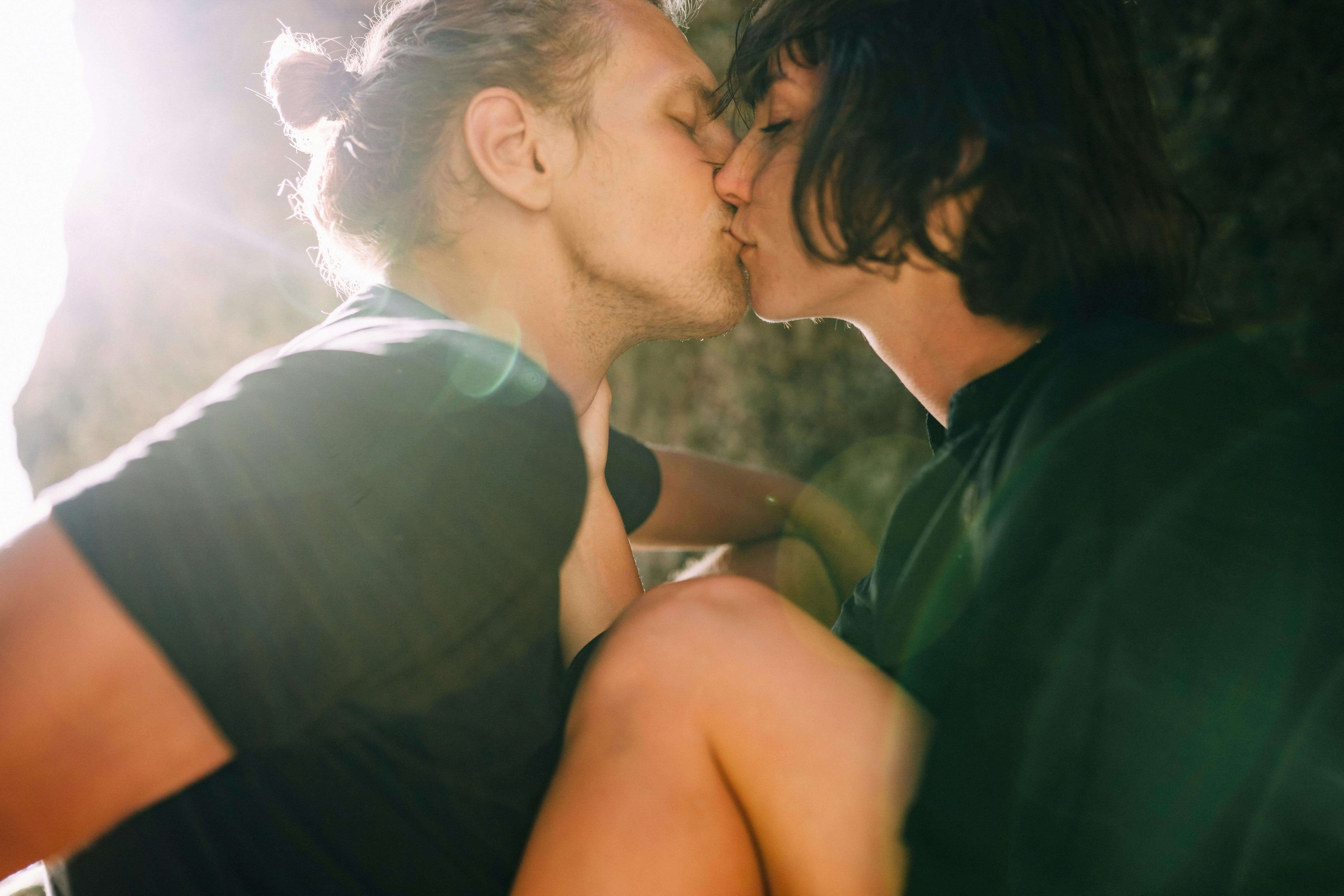 A tender moment captured between a couple kissing passionately in natural sunlight.