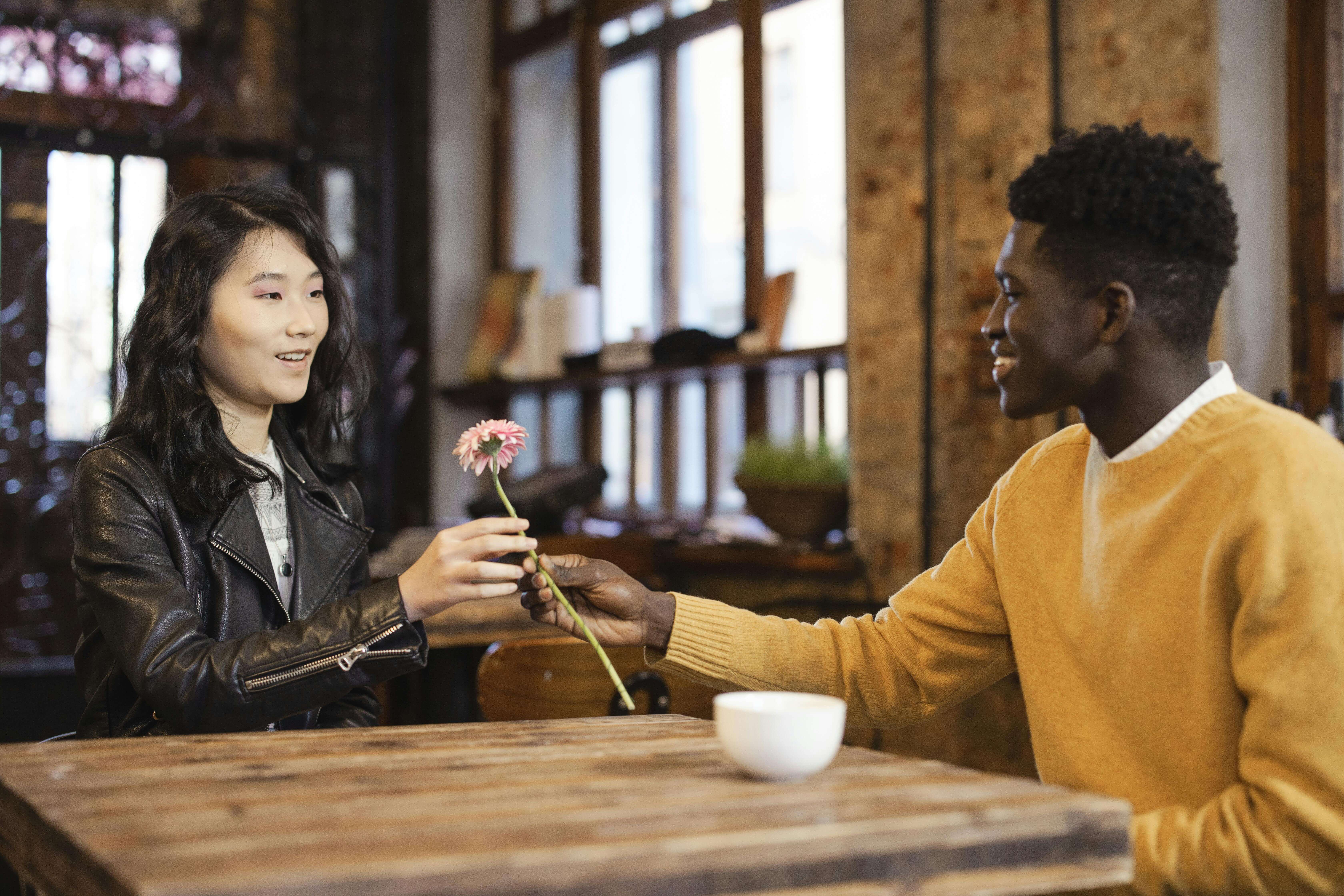 A warm scene of a couple exchanging a flower over a table in a cozy cafÃ©, symbolizing connection.