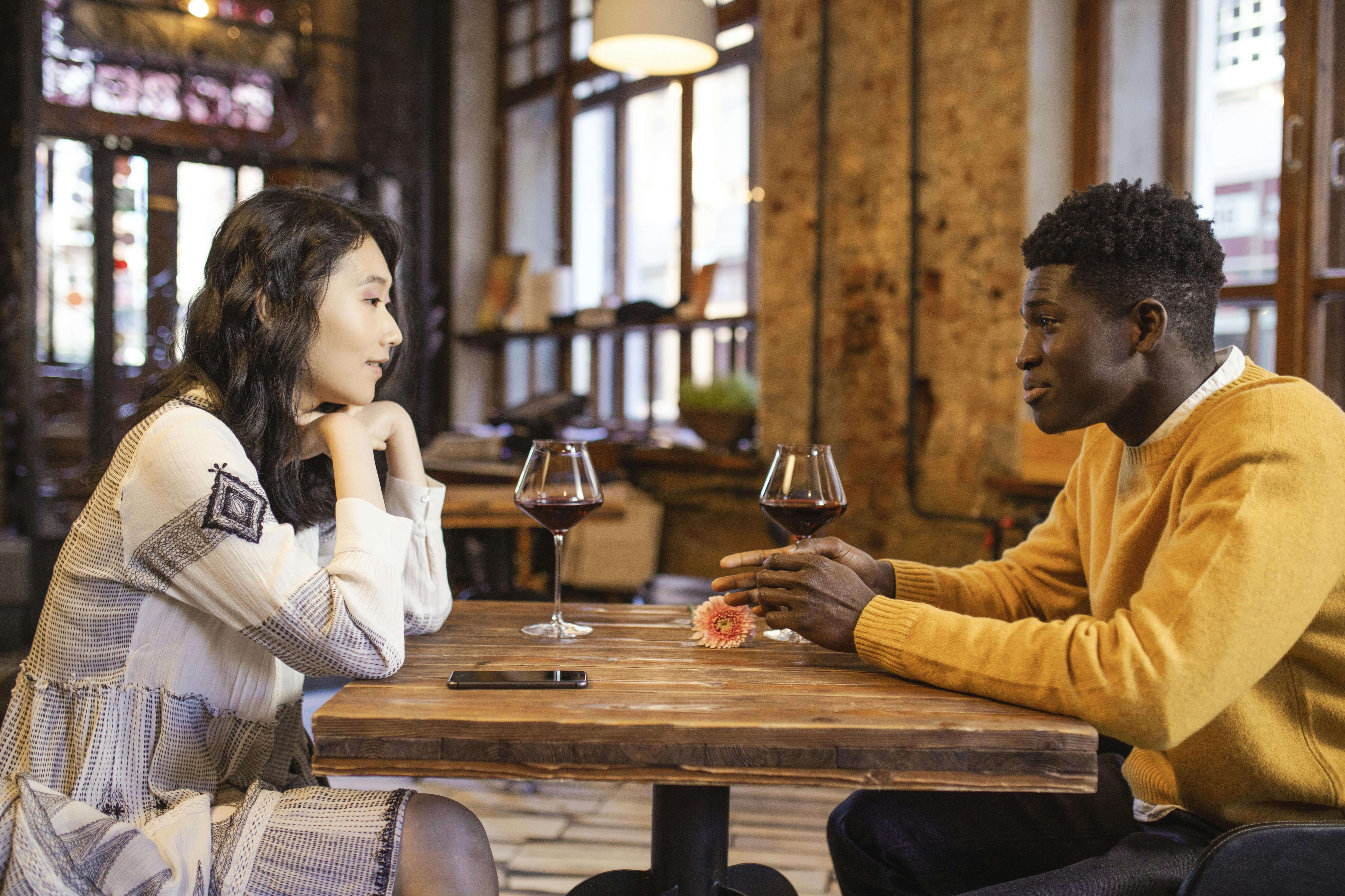 A couple enjoying a romantic date in a cozy cafÃ© with wine and engaging conversation.