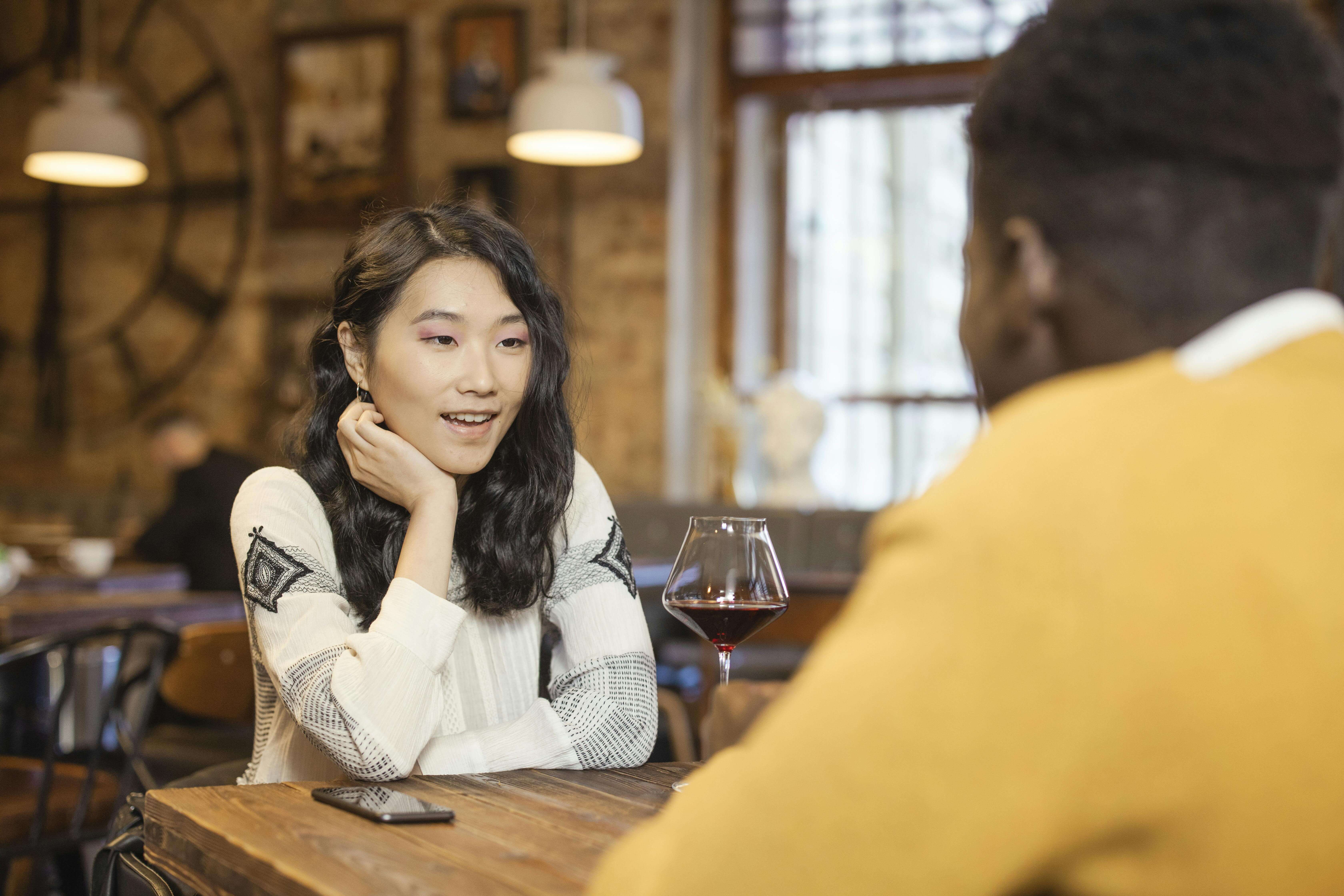 Two adults enjoying a conversation over wine in a warm, cozy café atmosphere.