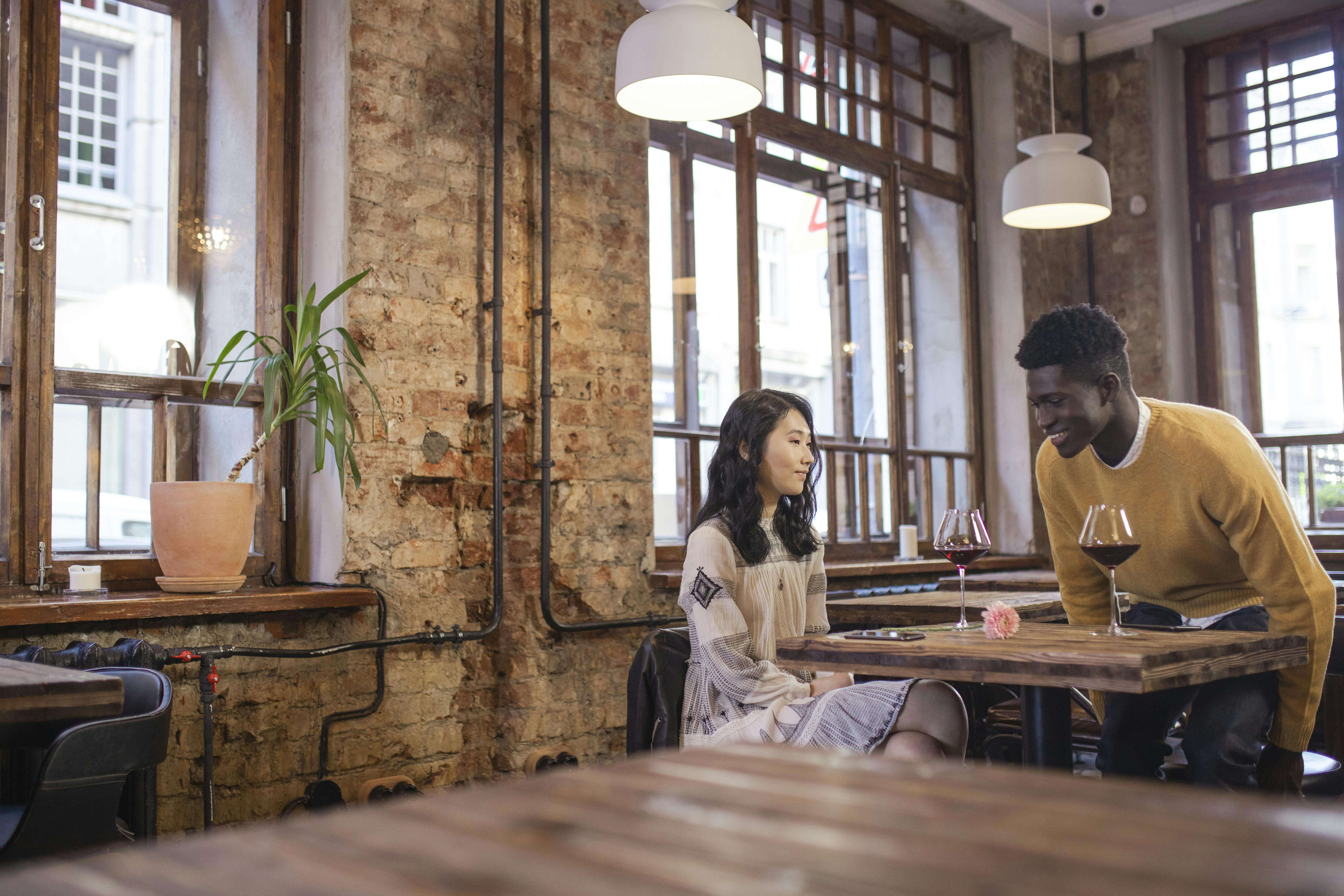A couple sharing a moment over wine in a cozy, rustic cafe with exposed brick walls.