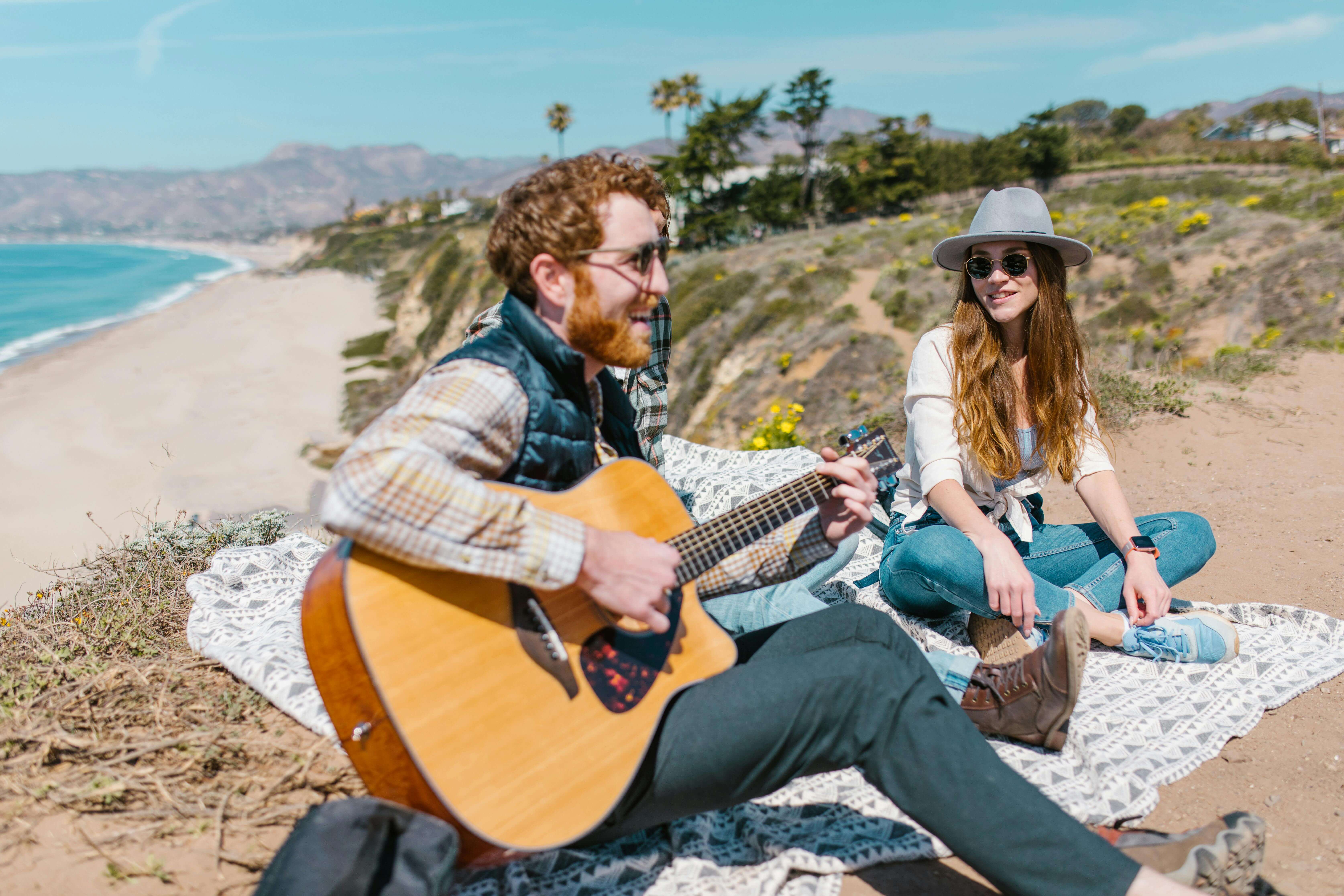 A joyful picnic on a sandy beach with friends, featuring a guitar and scenic ocean views.
