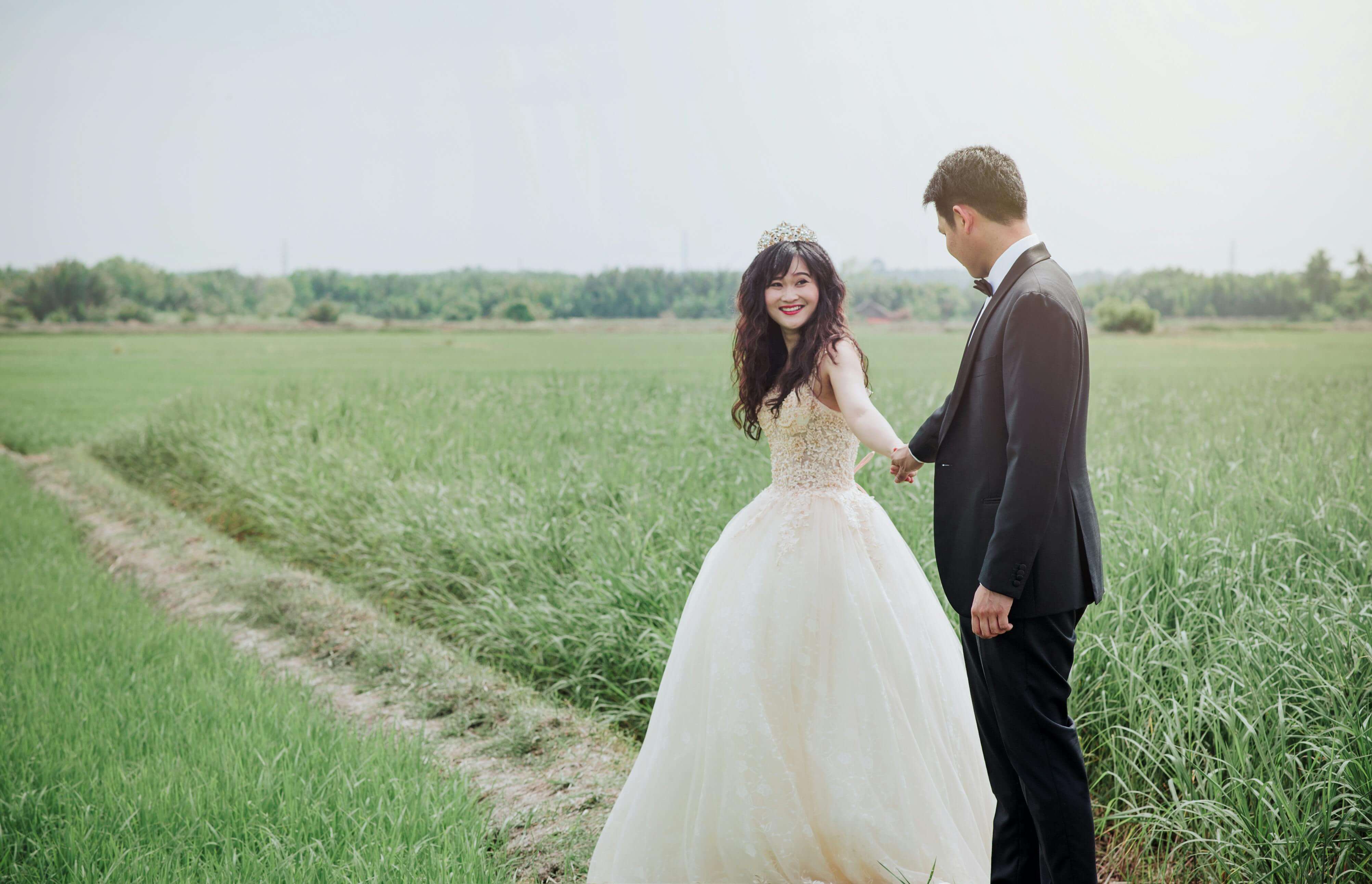 A joyful bride and groom holding hands in a green field, celebrating their love.