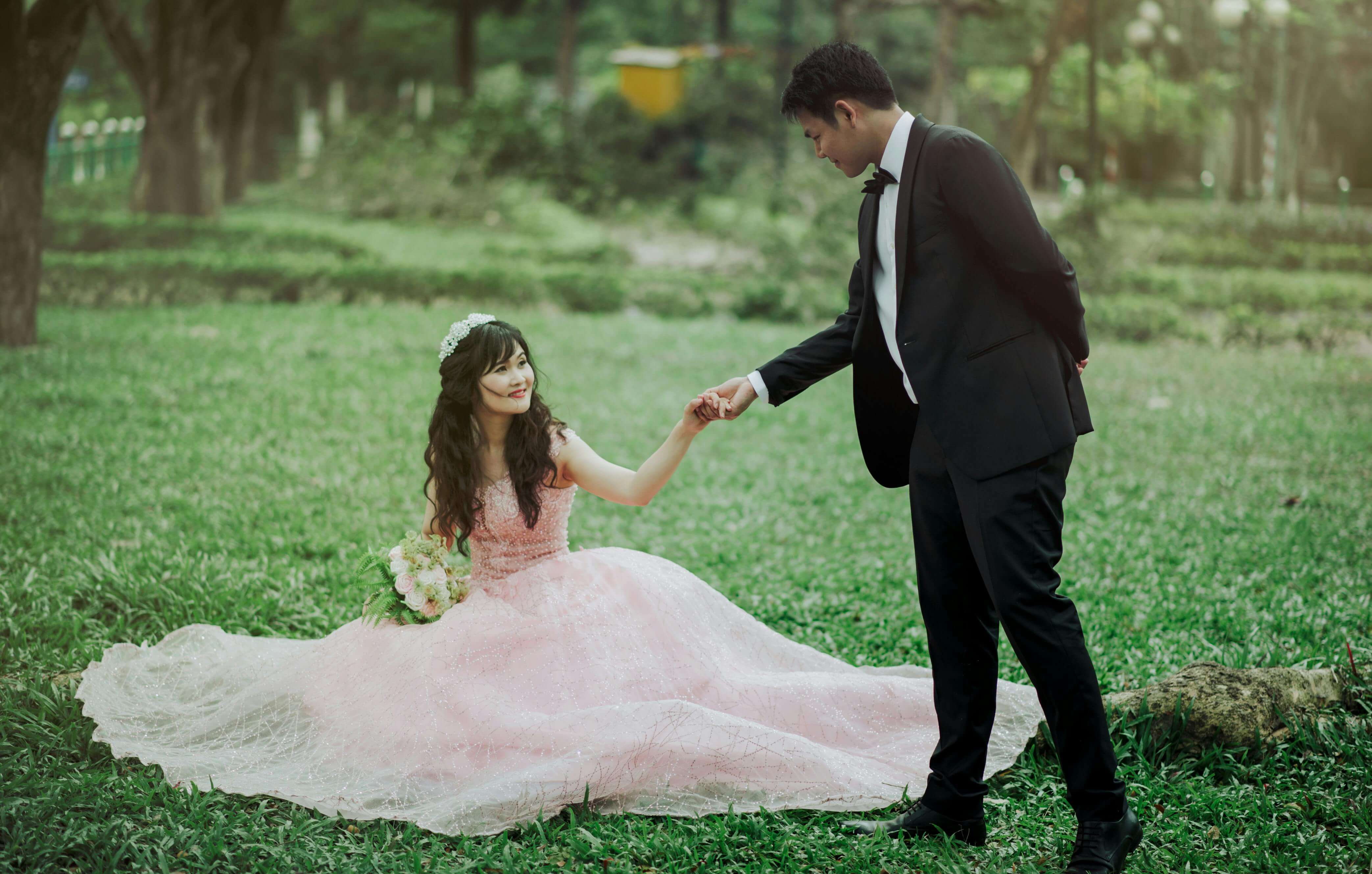 Lovely couple in wedding attire enjoying a romantic moment outdoors in a lush green park.