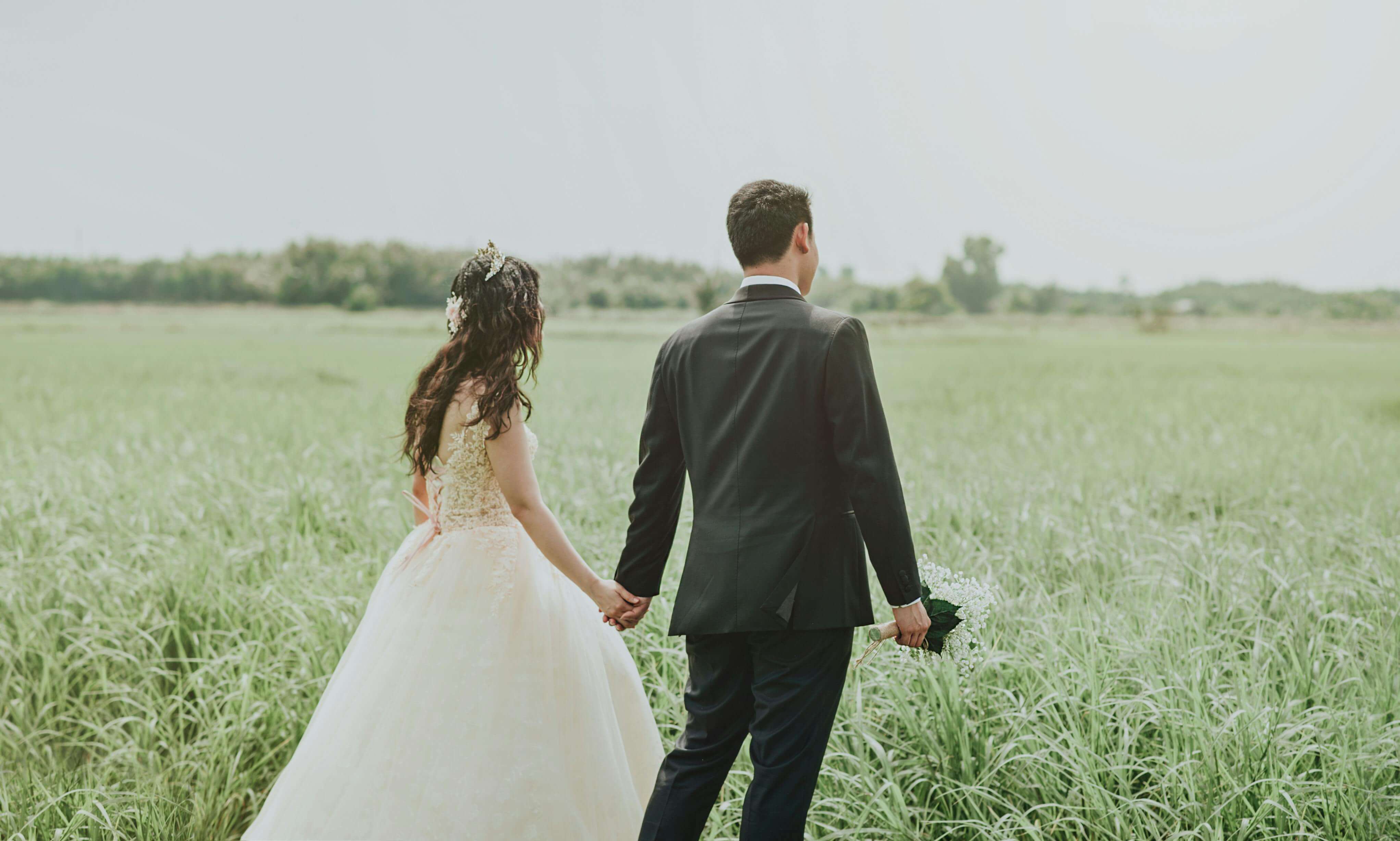 Couple holding hands in a serene field, perfect wedding photoshoot moment.