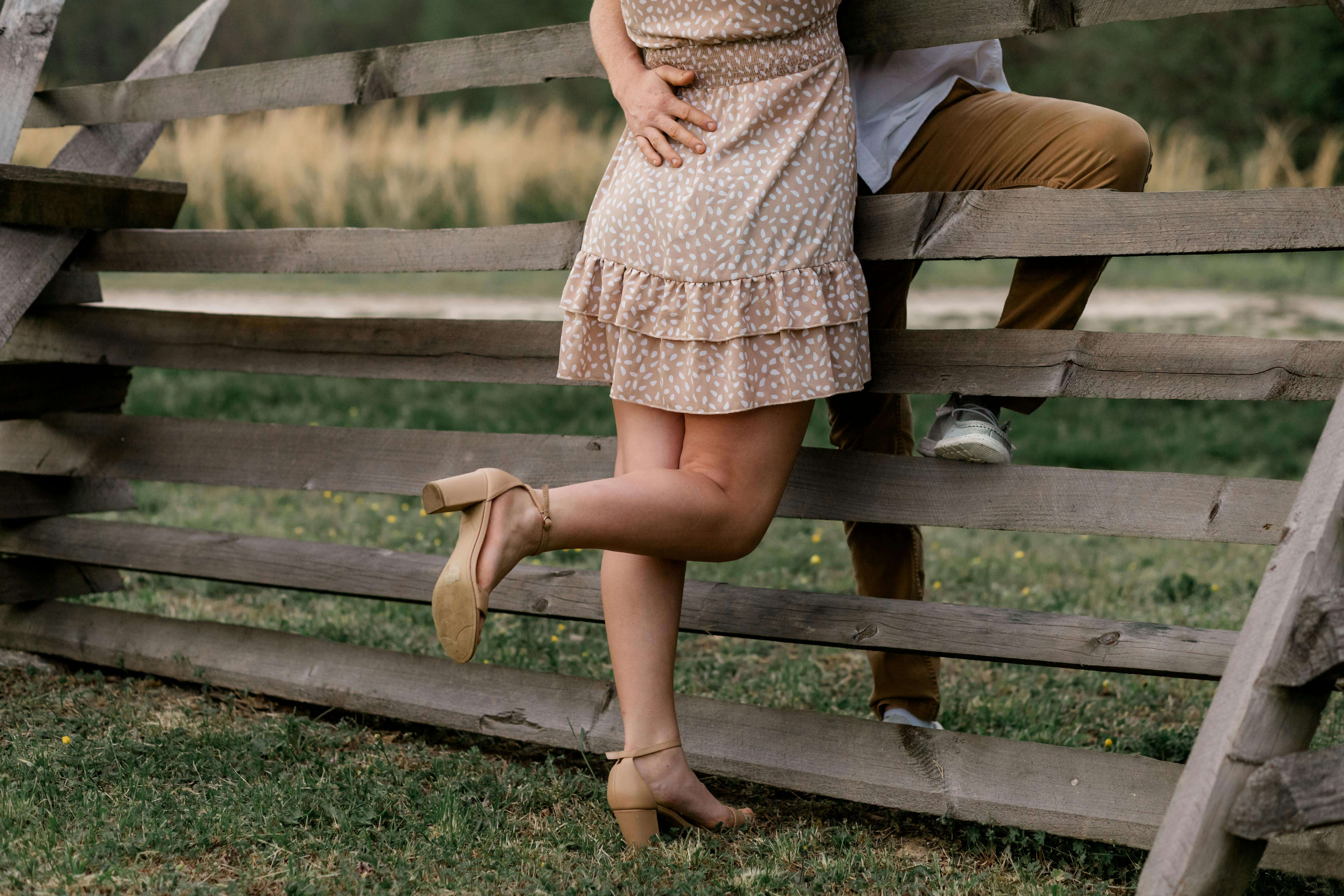 A couple's legs near a wooden fence, suggesting a romantic rural scene.