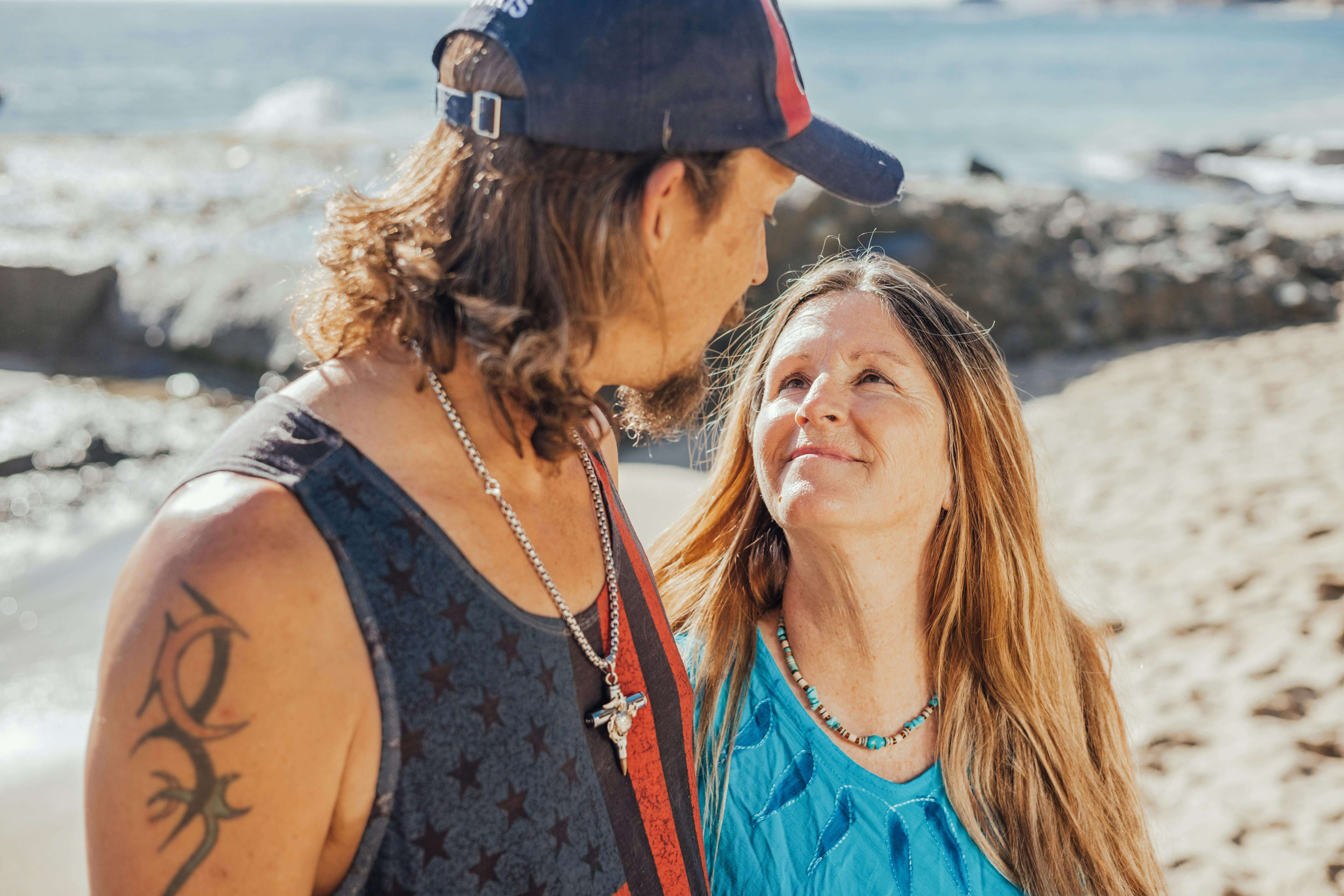 A happy couple gazes at each other lovingly during a sunny day at the beach.