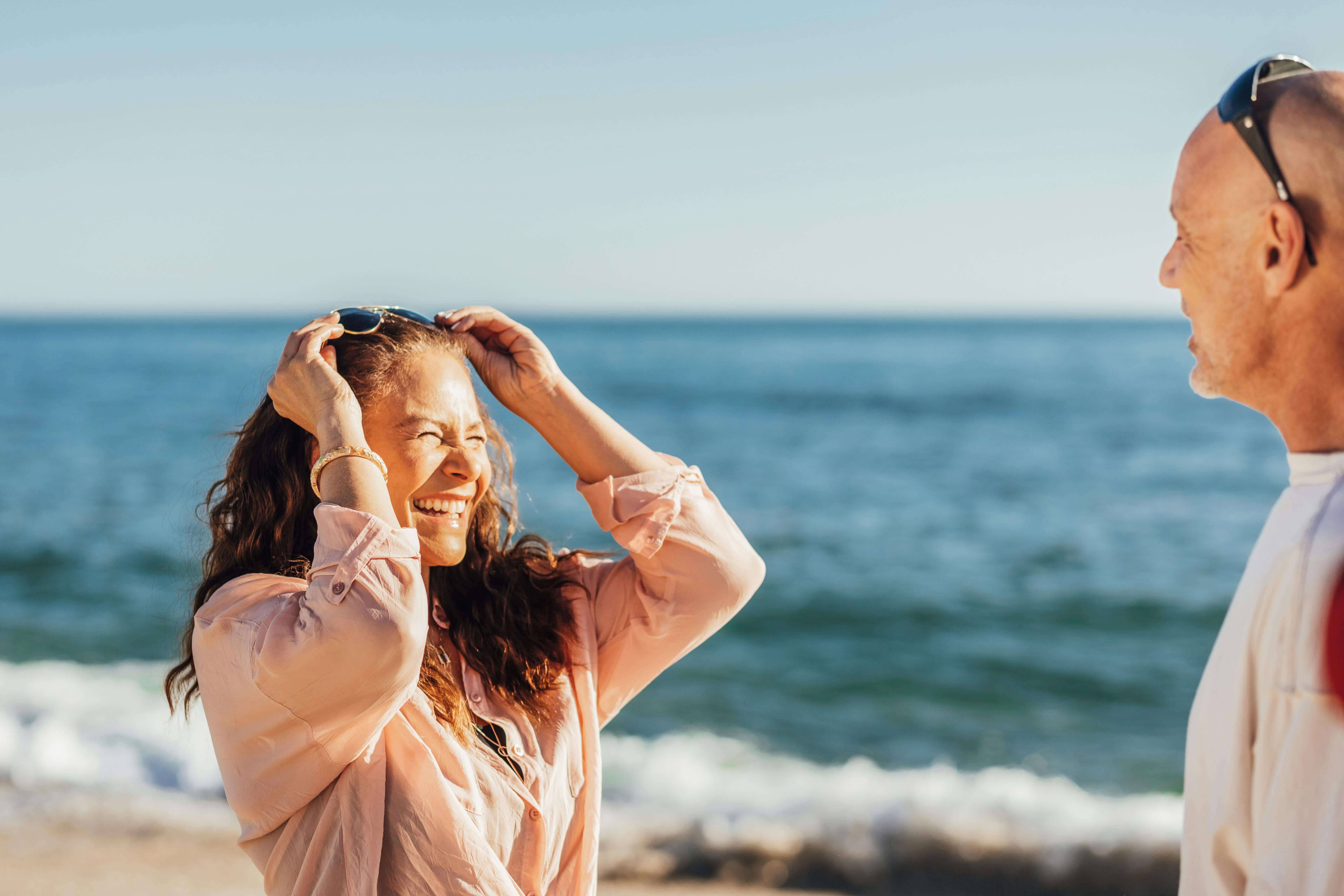 A cheerful couple enjoys a sunny day at the beach, laughing and relaxing by the sea.
