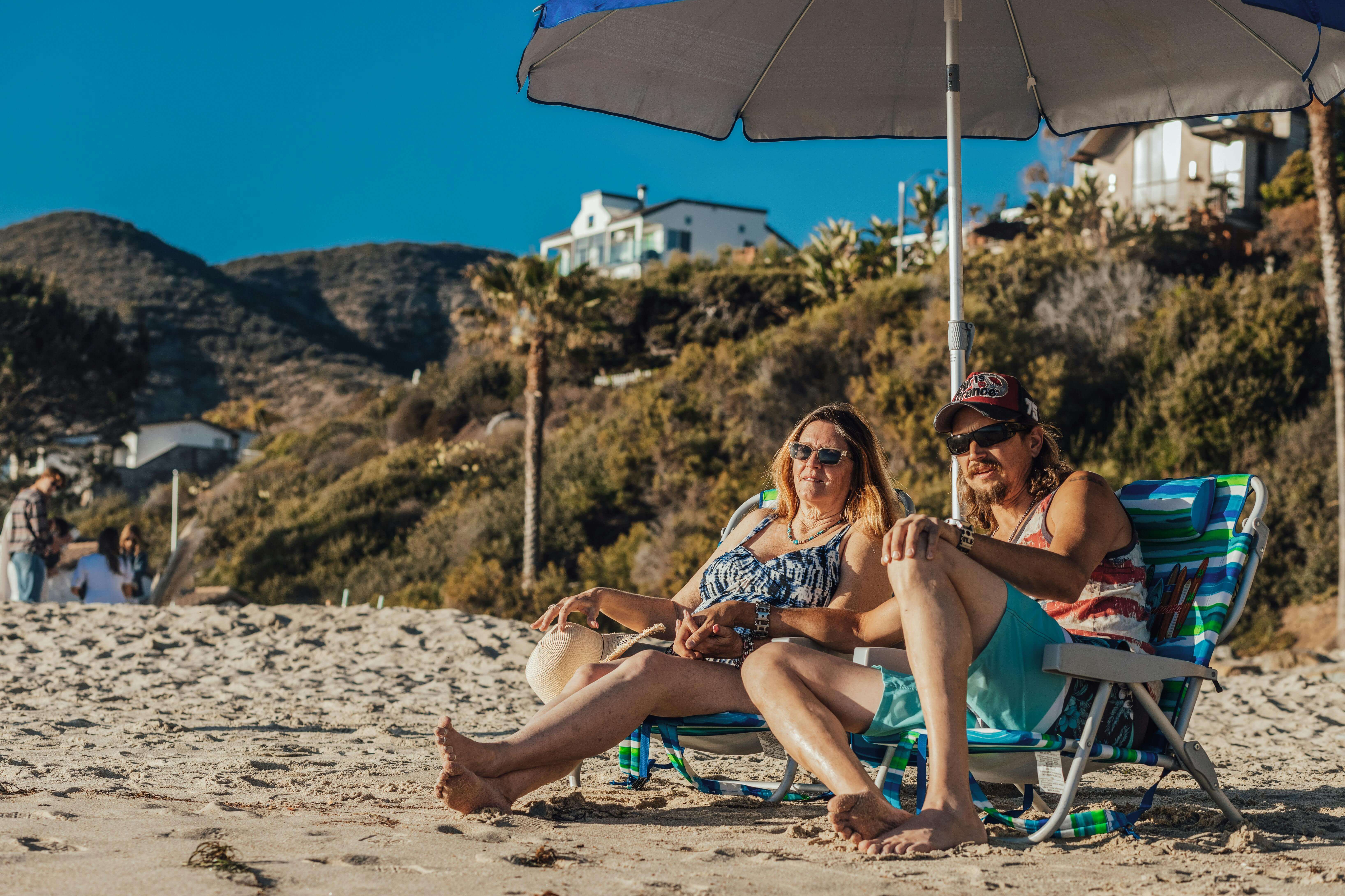 Couple enjoying a sunny day on the beach under an umbrella, capturing summer relaxation.