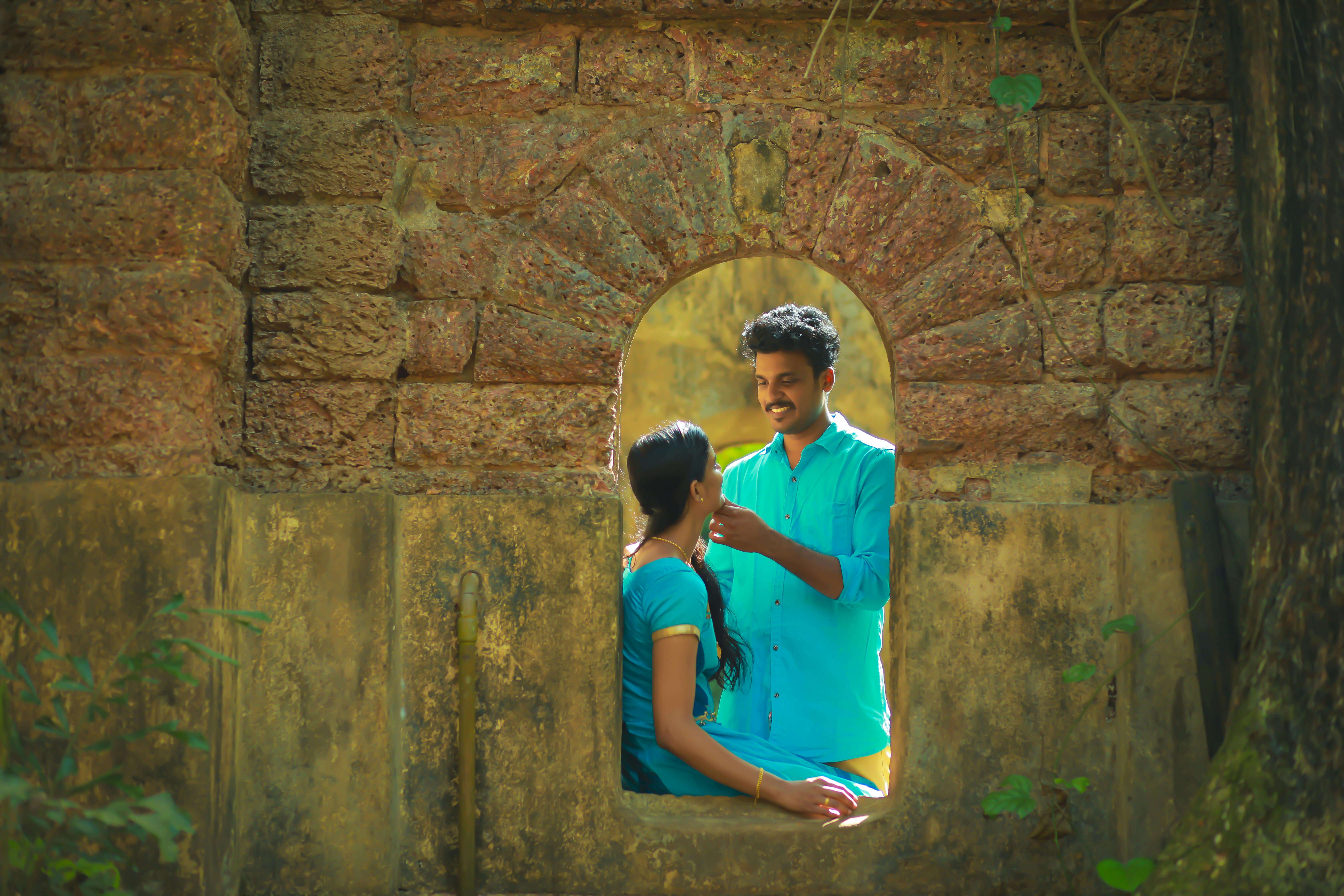 A couple sharing a moment by a rustic arched window framed by brick walls.