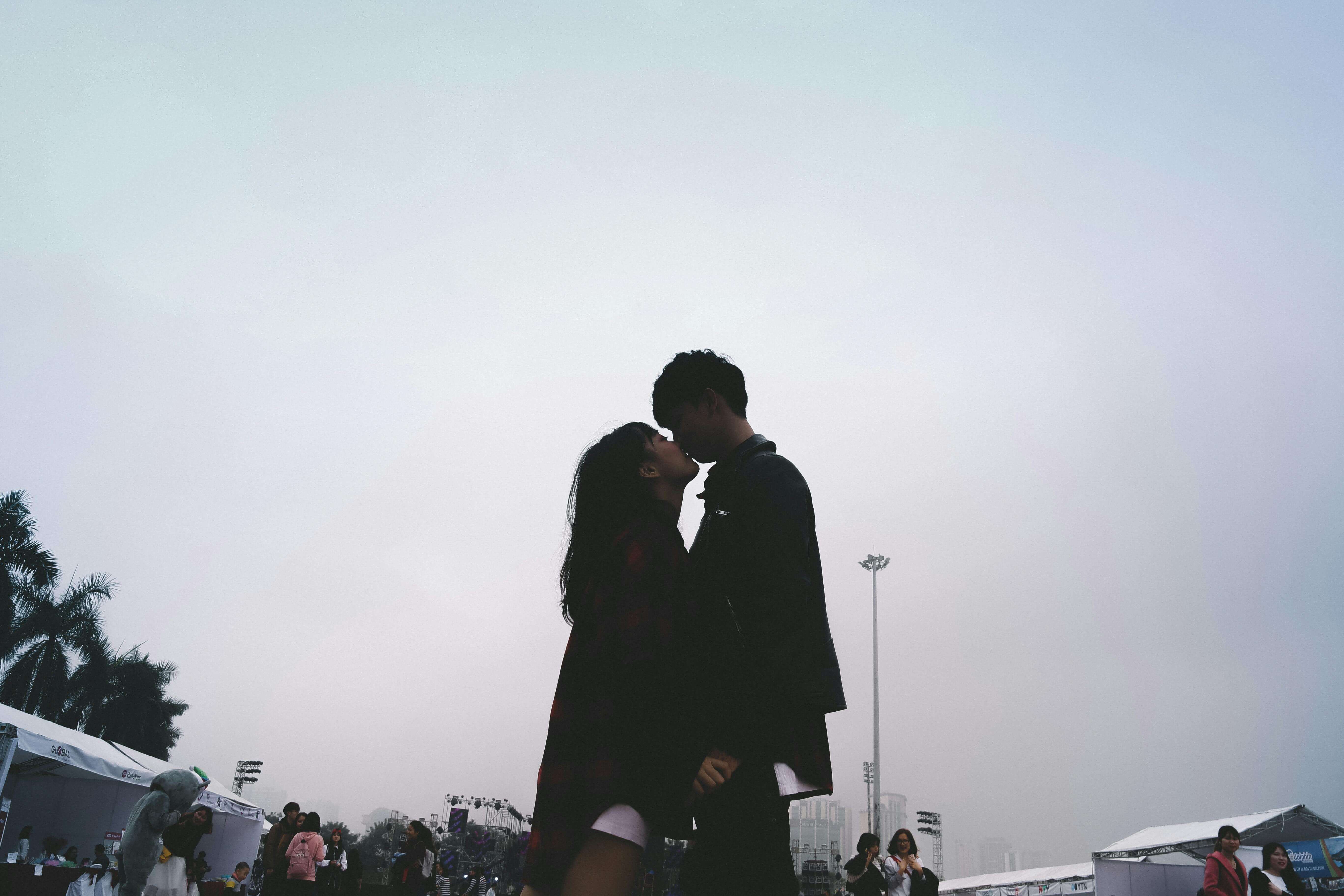 A romantic silhouette of a couple kissing outdoors during a daytime festival in Hanoi, Vietnam.