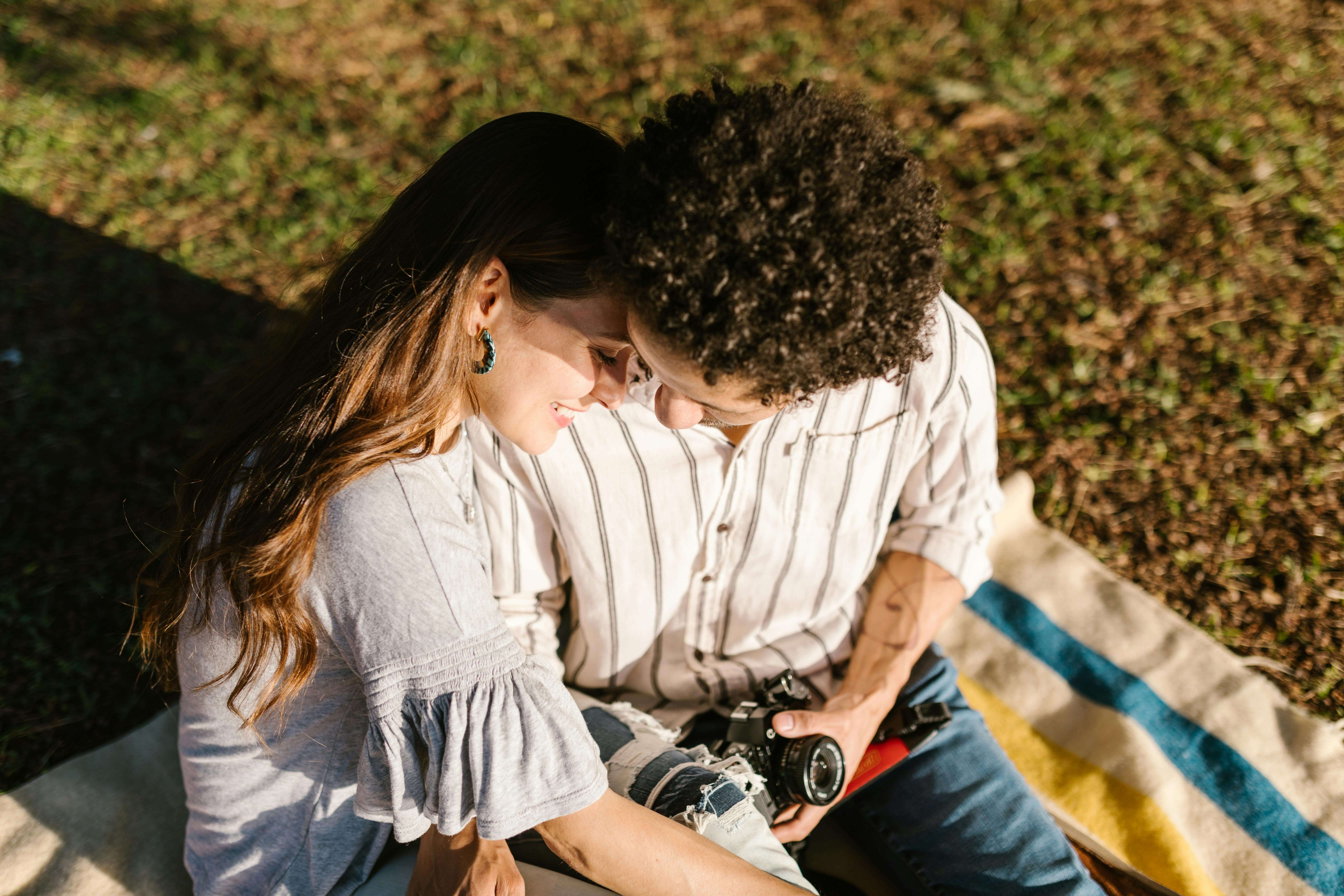 A loving couple sitting closely on a blanket outdoors, sharing an intimate moment.