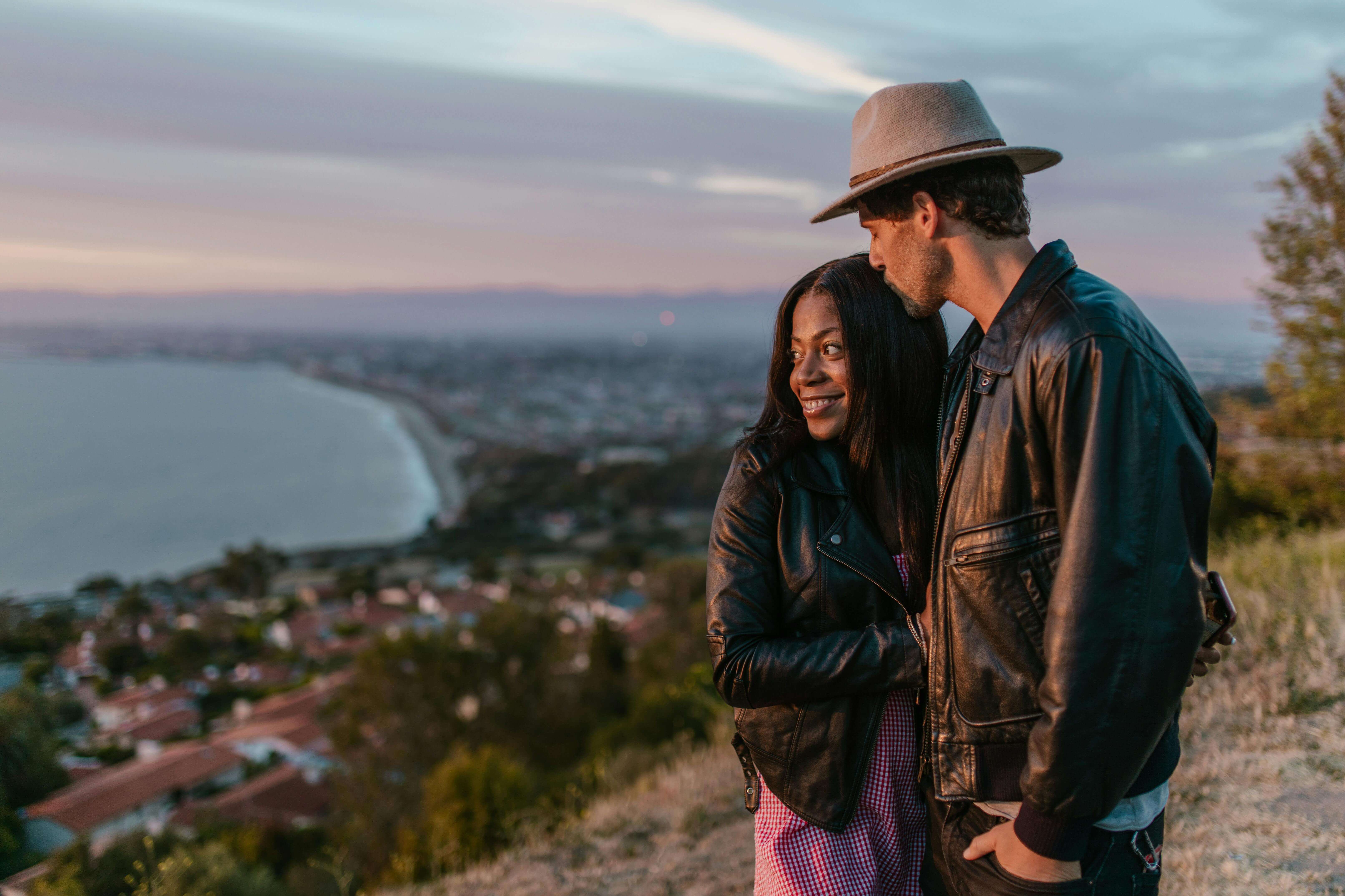 Couple embraces with a stunning coastal sunset backdrop, exuding romance and affection.