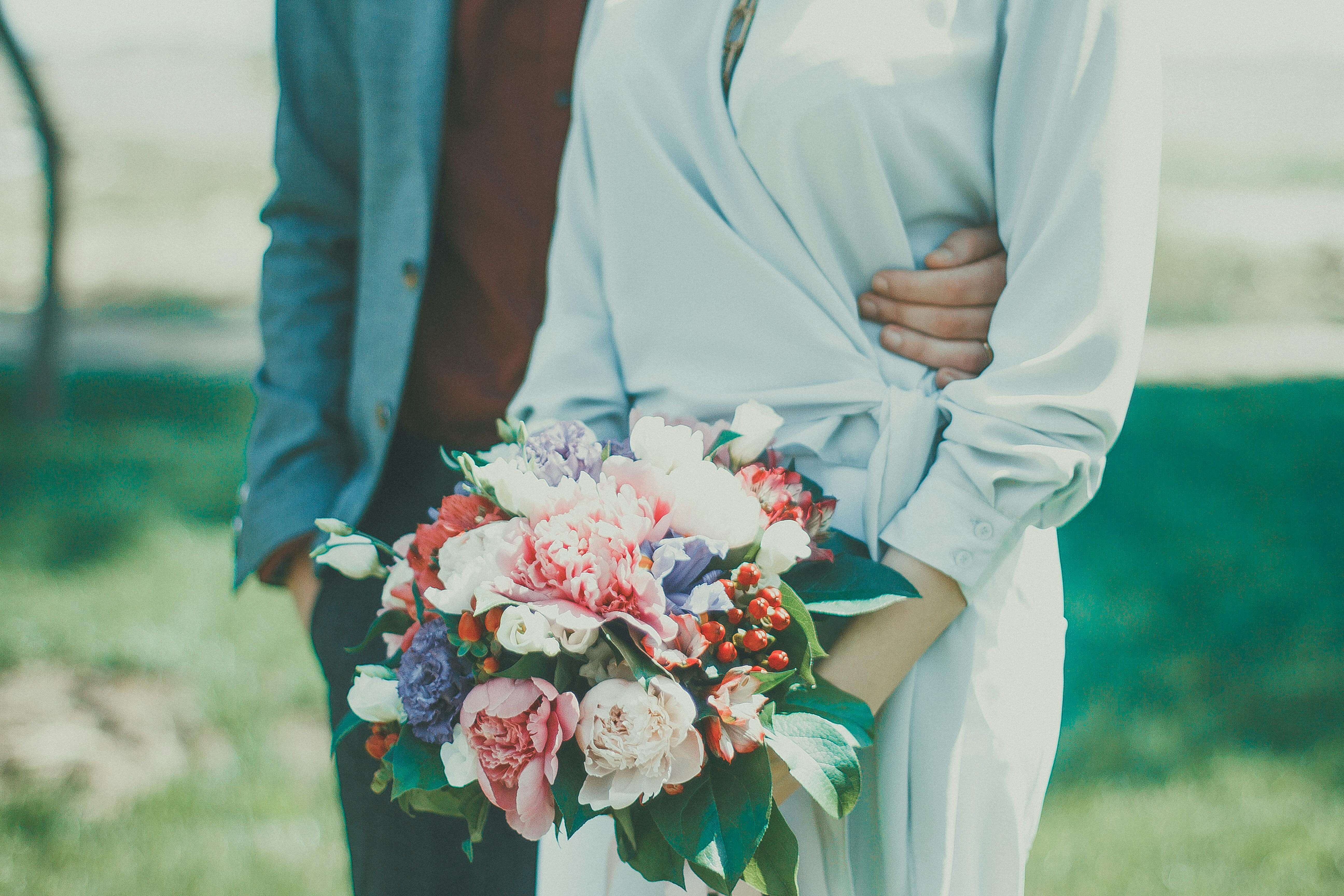 Elegant outdoor wedding photo with bride and groom holding a colorful flower bouquet, perfect for romantic and summer themes.