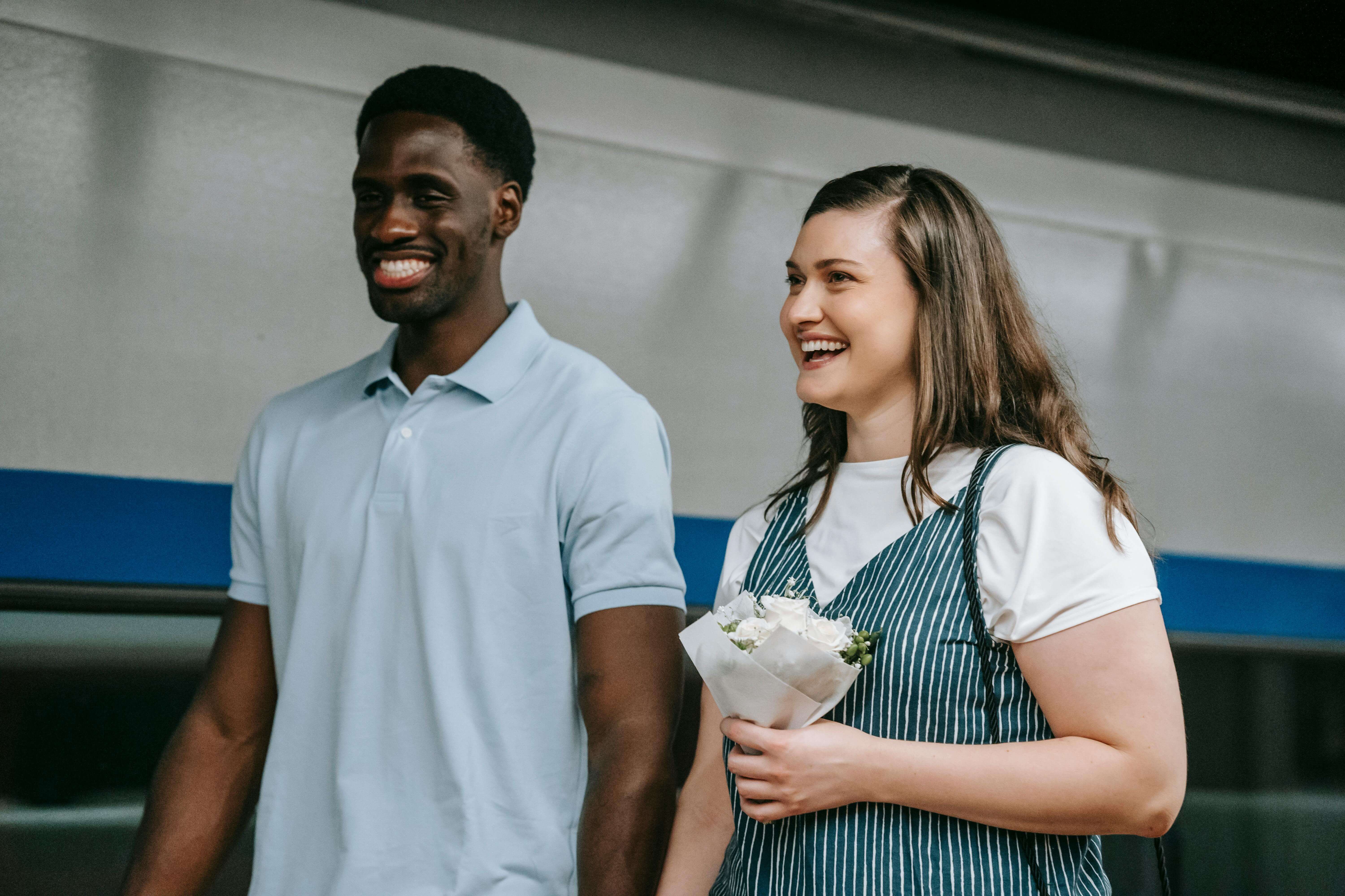 A cheerful interracial couple holding flowers, captured indoors, showcasing love and joy.