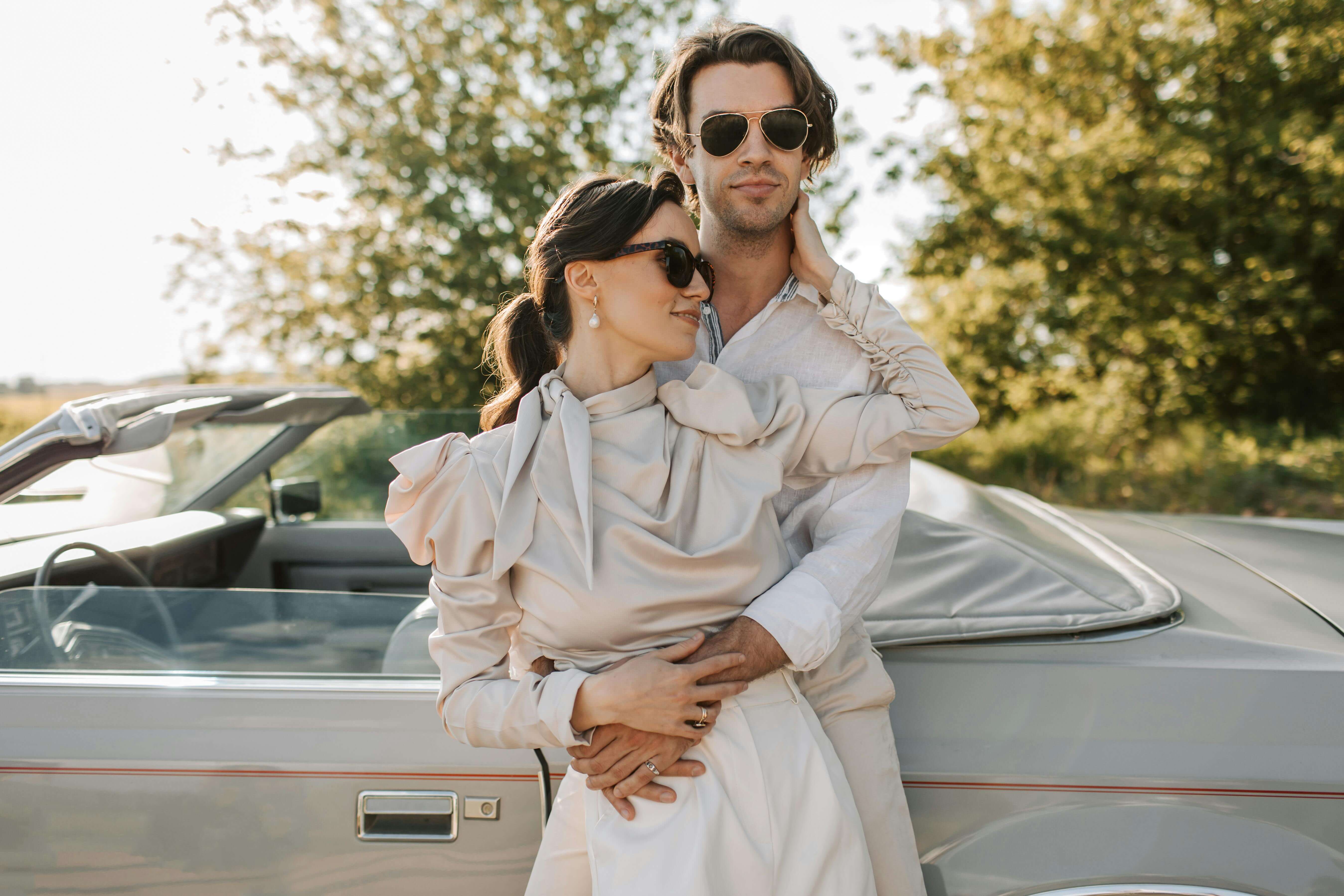 Elegant couple embracing by convertible car on a sunny day, radiating romance