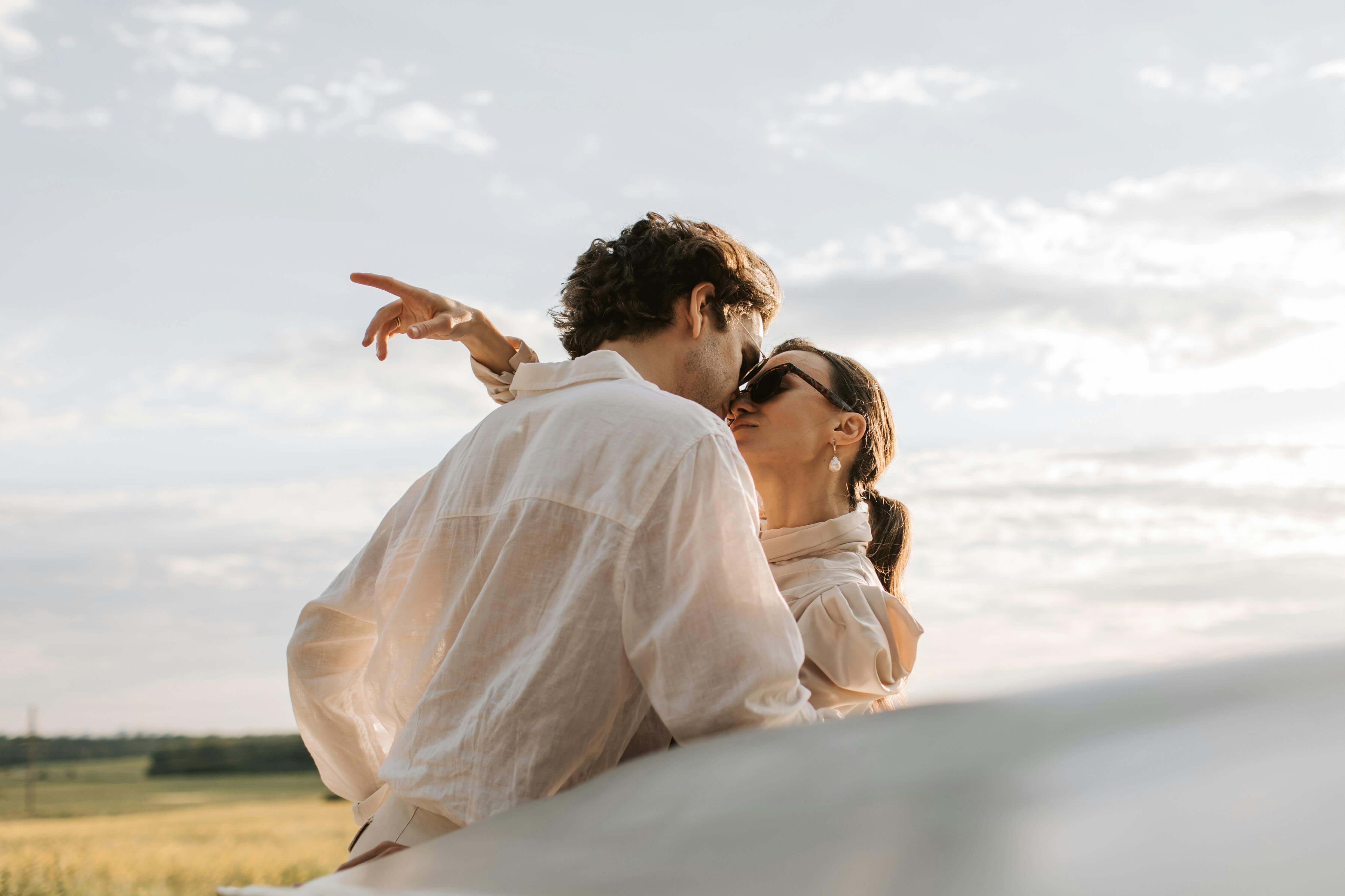 A couple shares a romantic moment outdoors with a warm sunset backdrop, expressing love and affection.