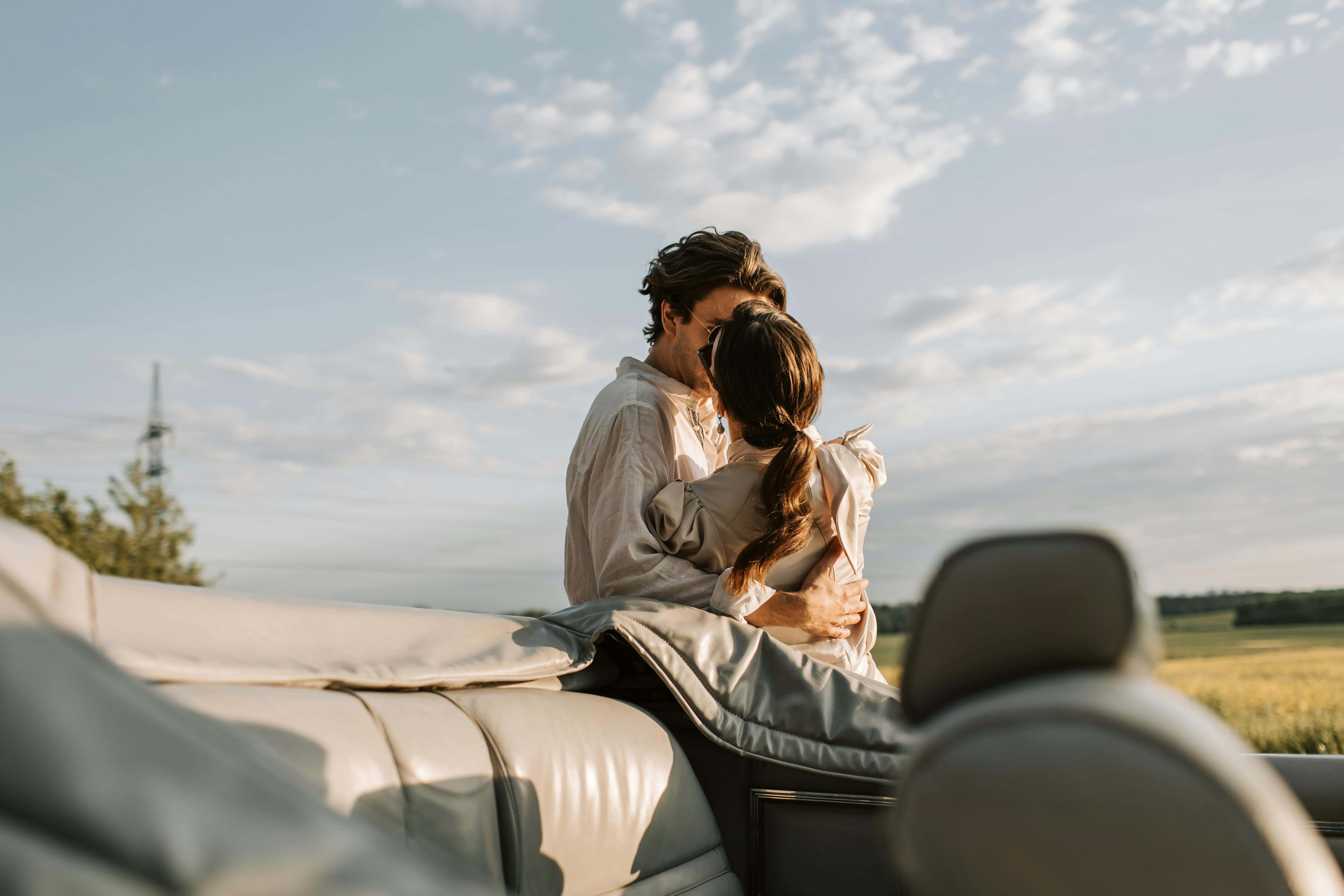 A couple sharing a romantic moment in a convertible car under a clear sky, showcasing intimacy and love.