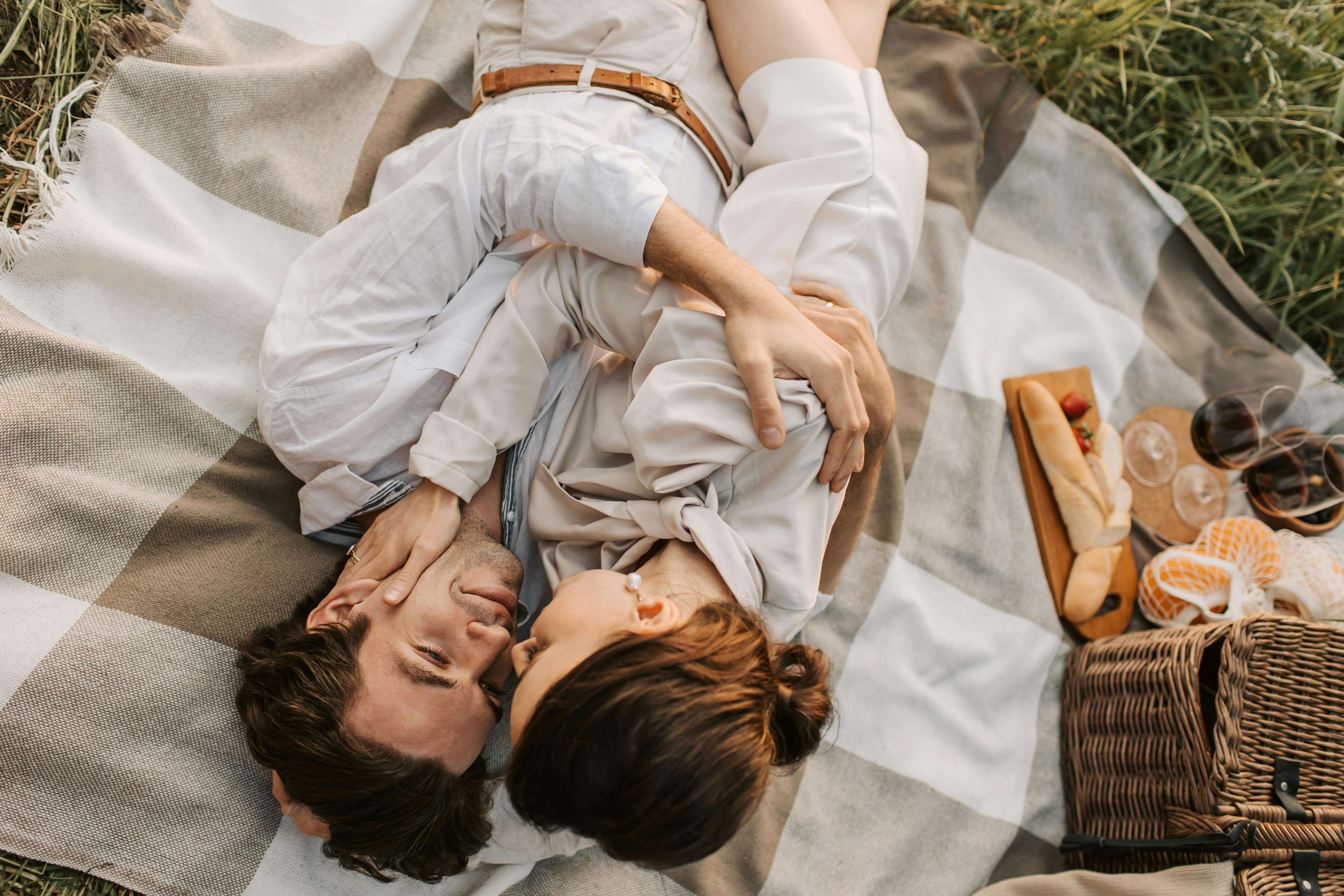 A couple shares a tender moment during a picnic on a checkered blanket in a grassy field.
