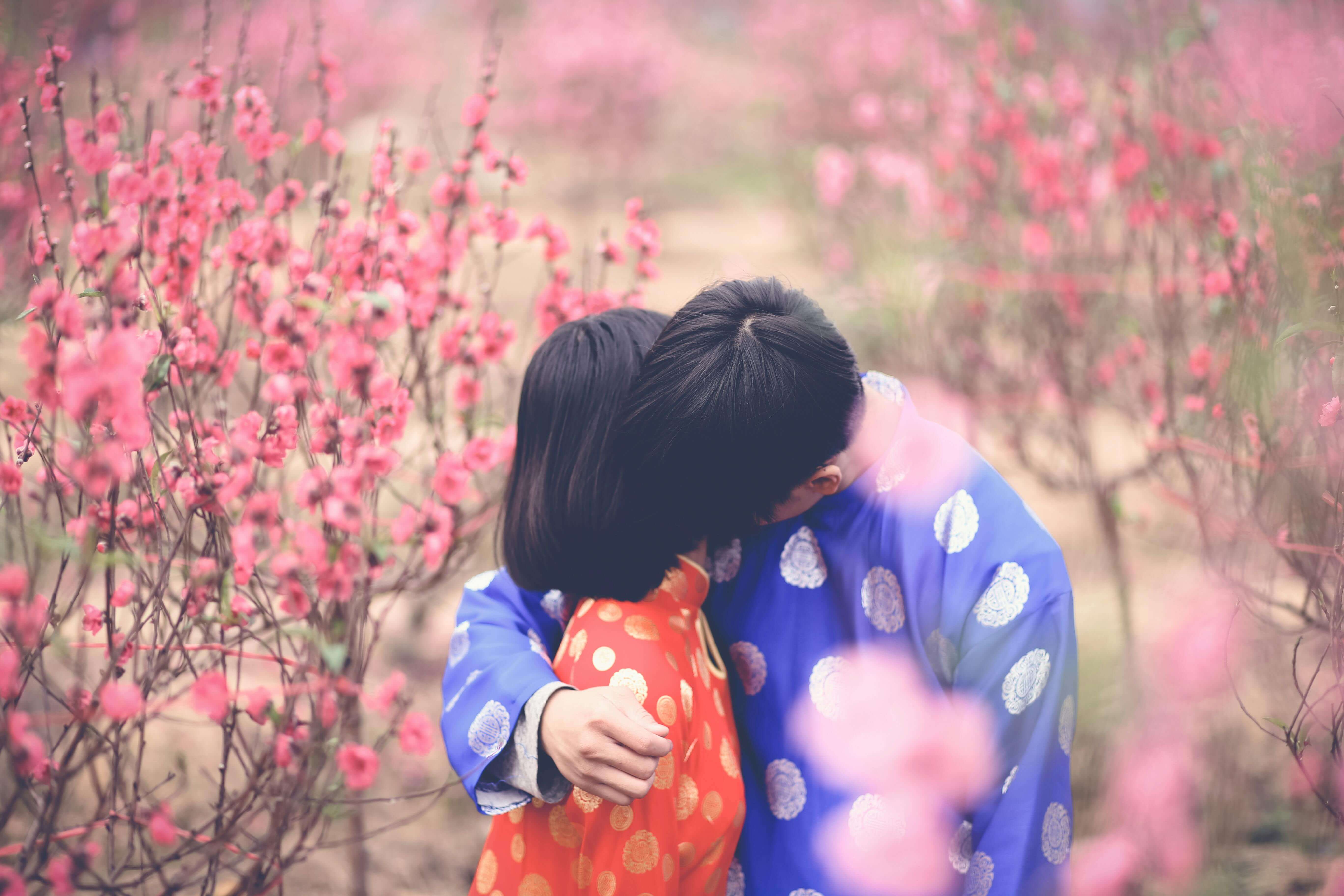 Couple in colorful traditional attire sharing a loving embrace in a flower garden.