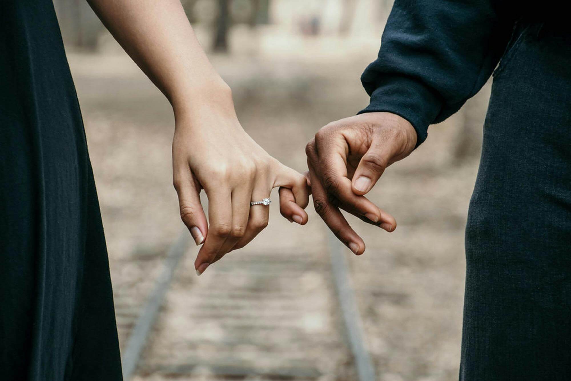 A romantic couple holding hands, symbolizing love and unity on a scenic railtrack.