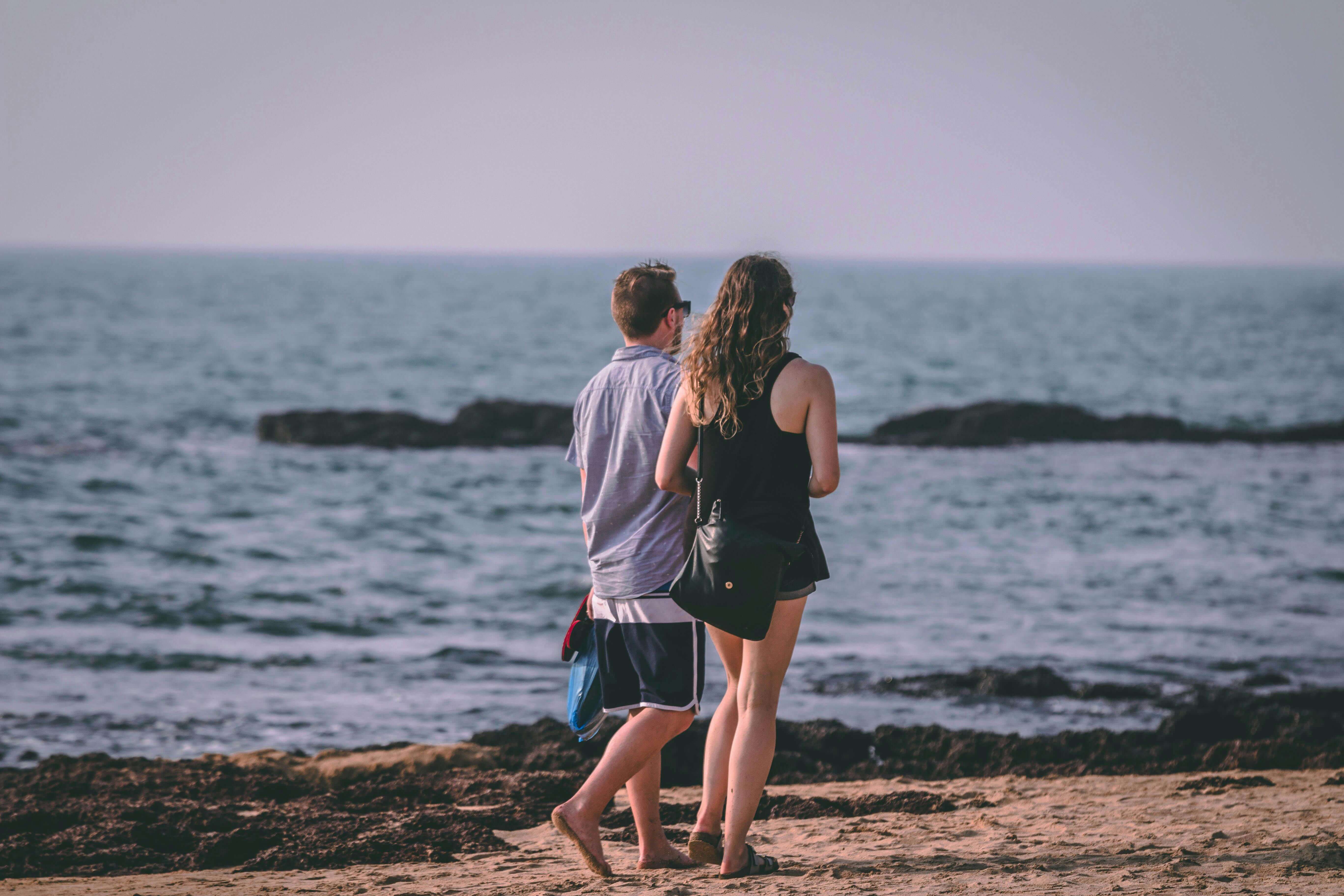 A couple enjoys a romantic walk on a sandy beach by the ocean, capturing leisure and love.