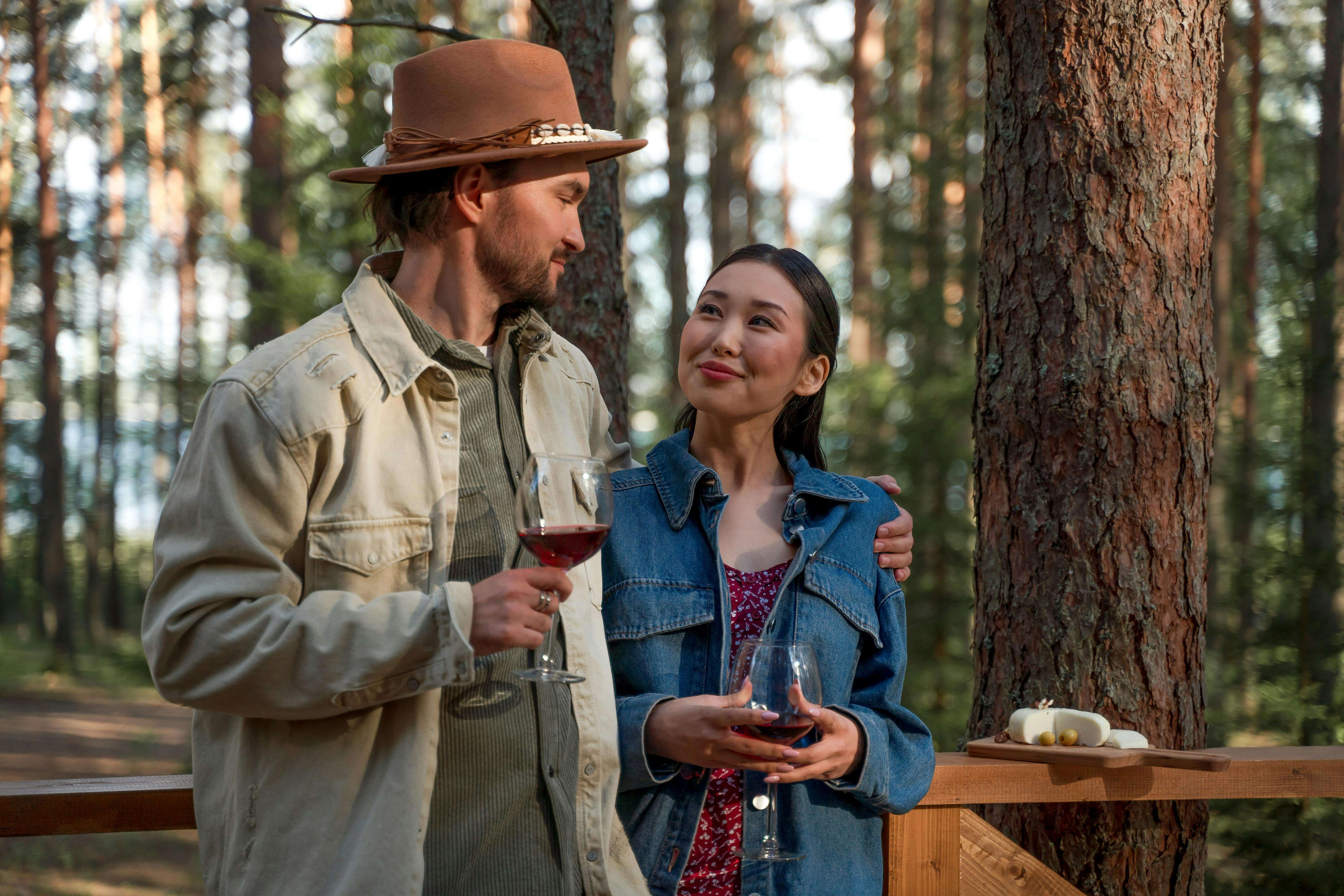 A couple shares a romantic moment drinking wine in a serene forest setting.
