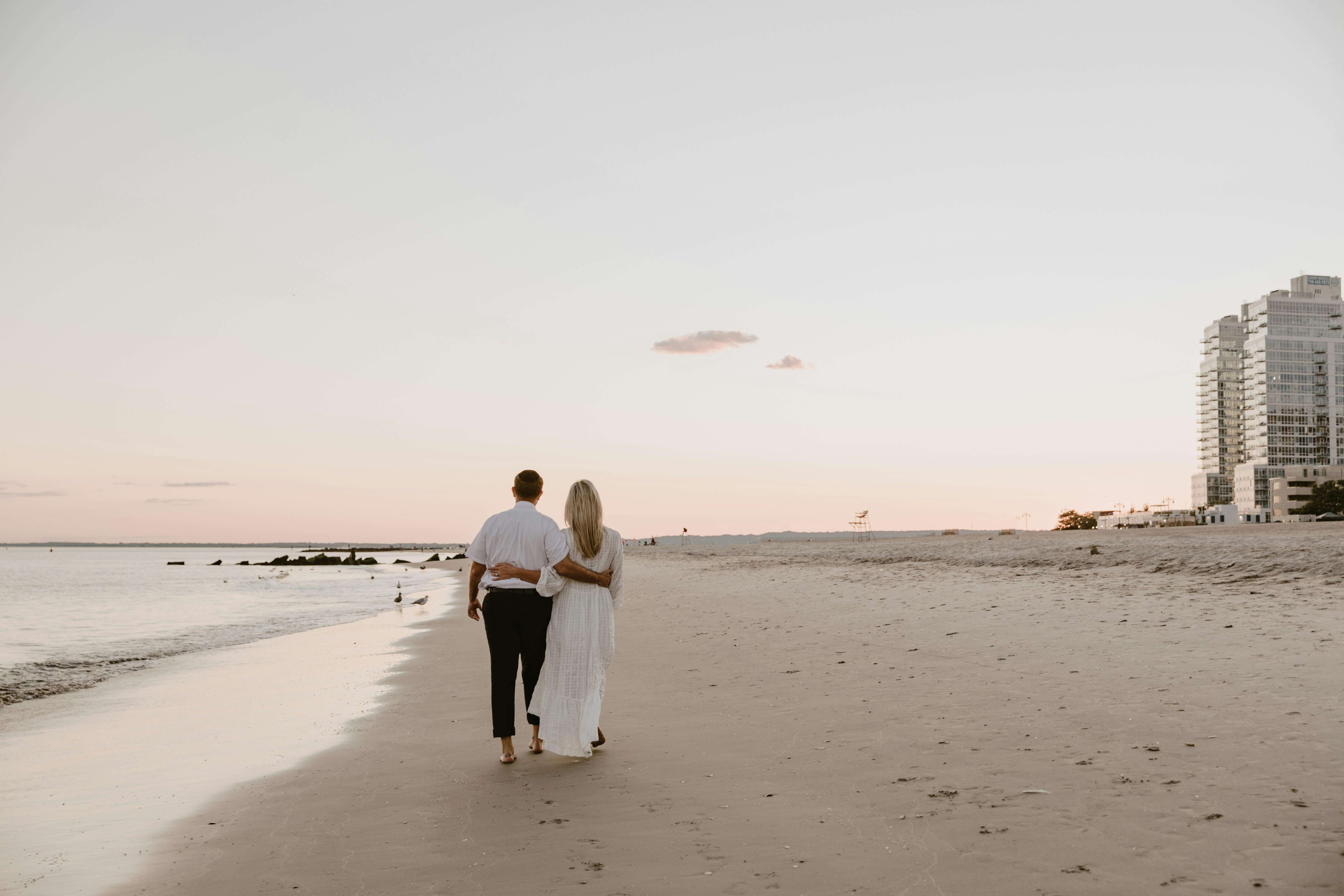 A couple walks arm in arm along a serene beach at sunset, conveying romance and tranquility.