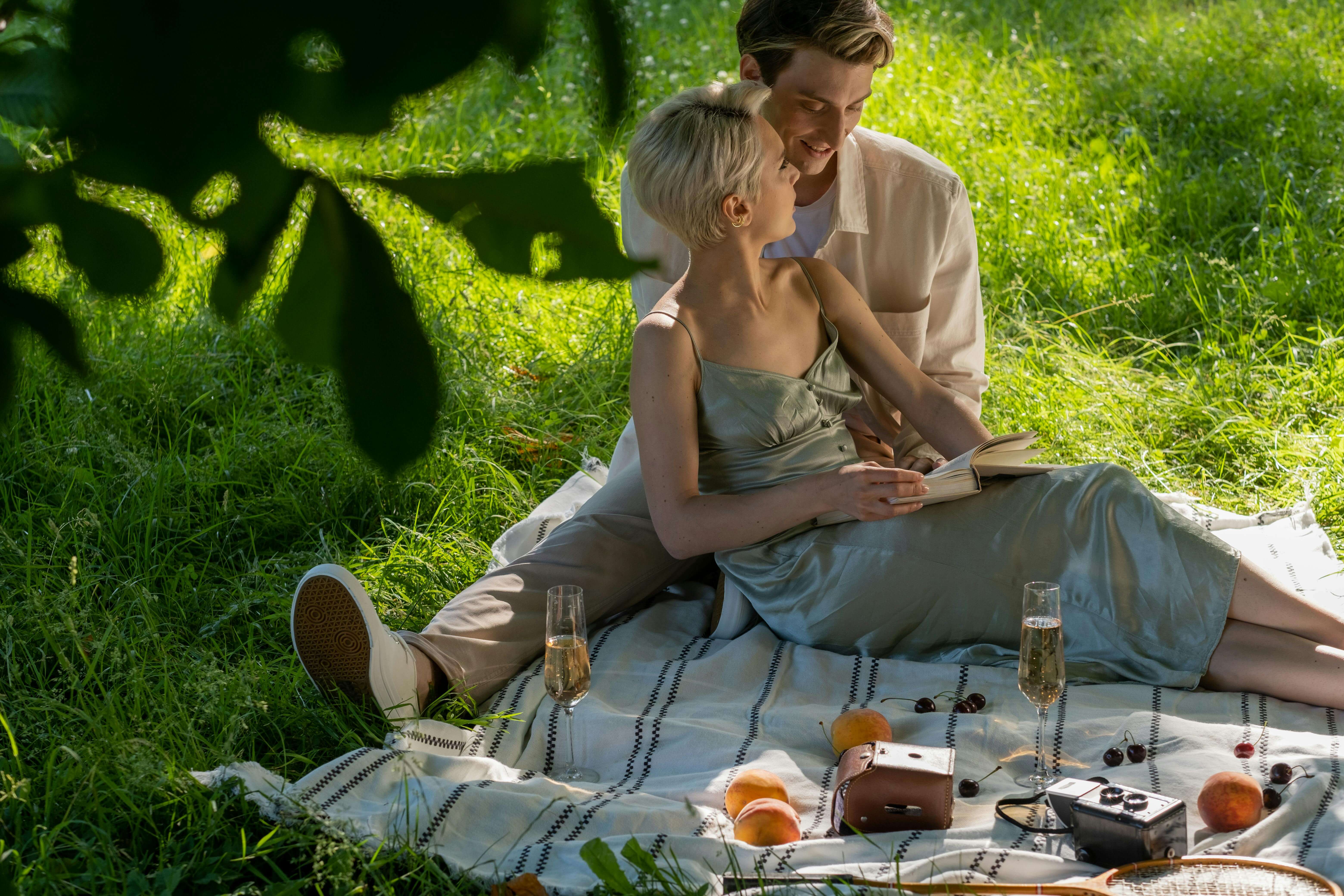 A couple shares a romantic picnic outdoors with champagne and fresh fruits on a sunny day.