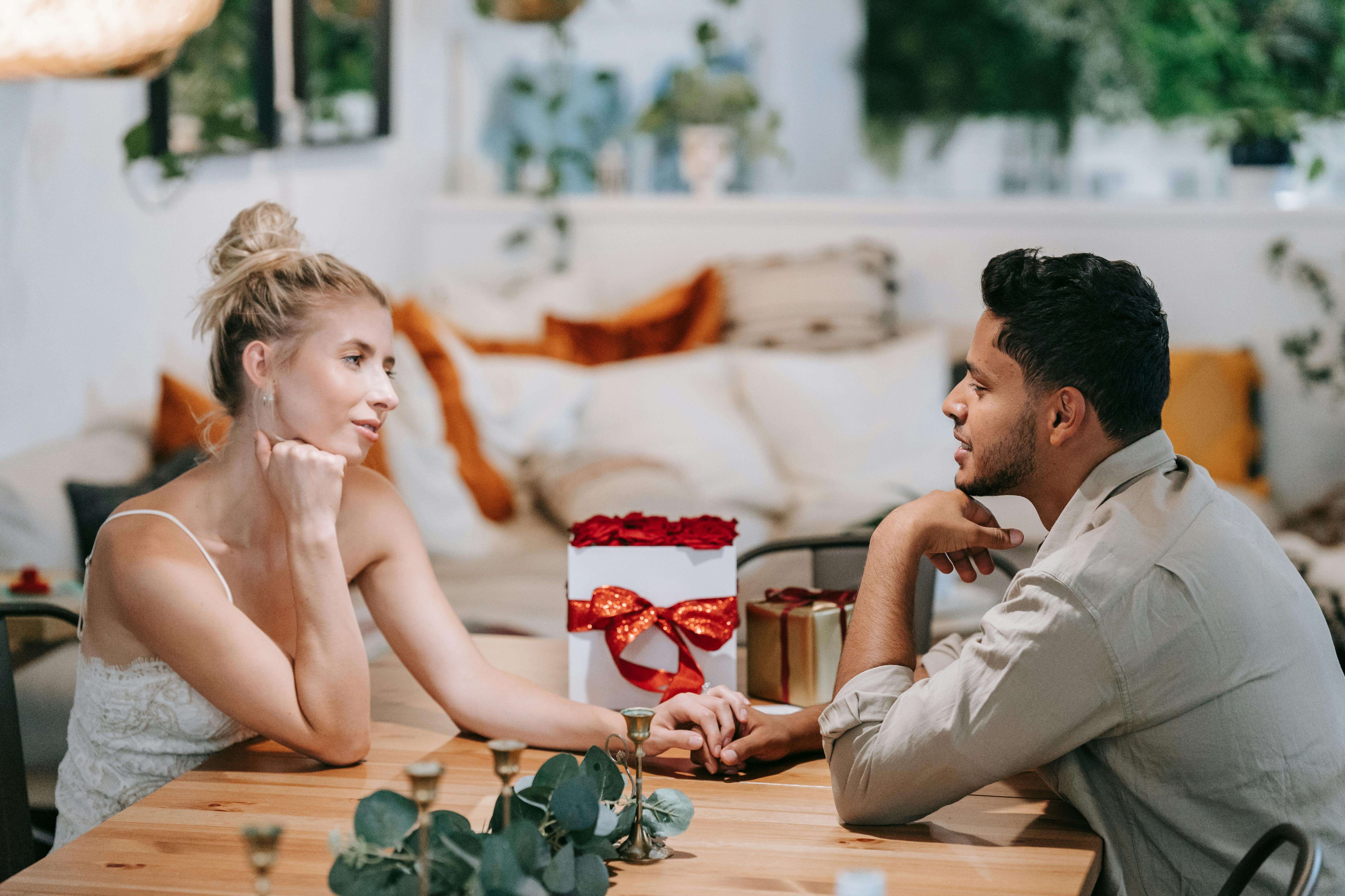 A loving couple enjoying a romantic date, holding hands indoors with a gift on the table.