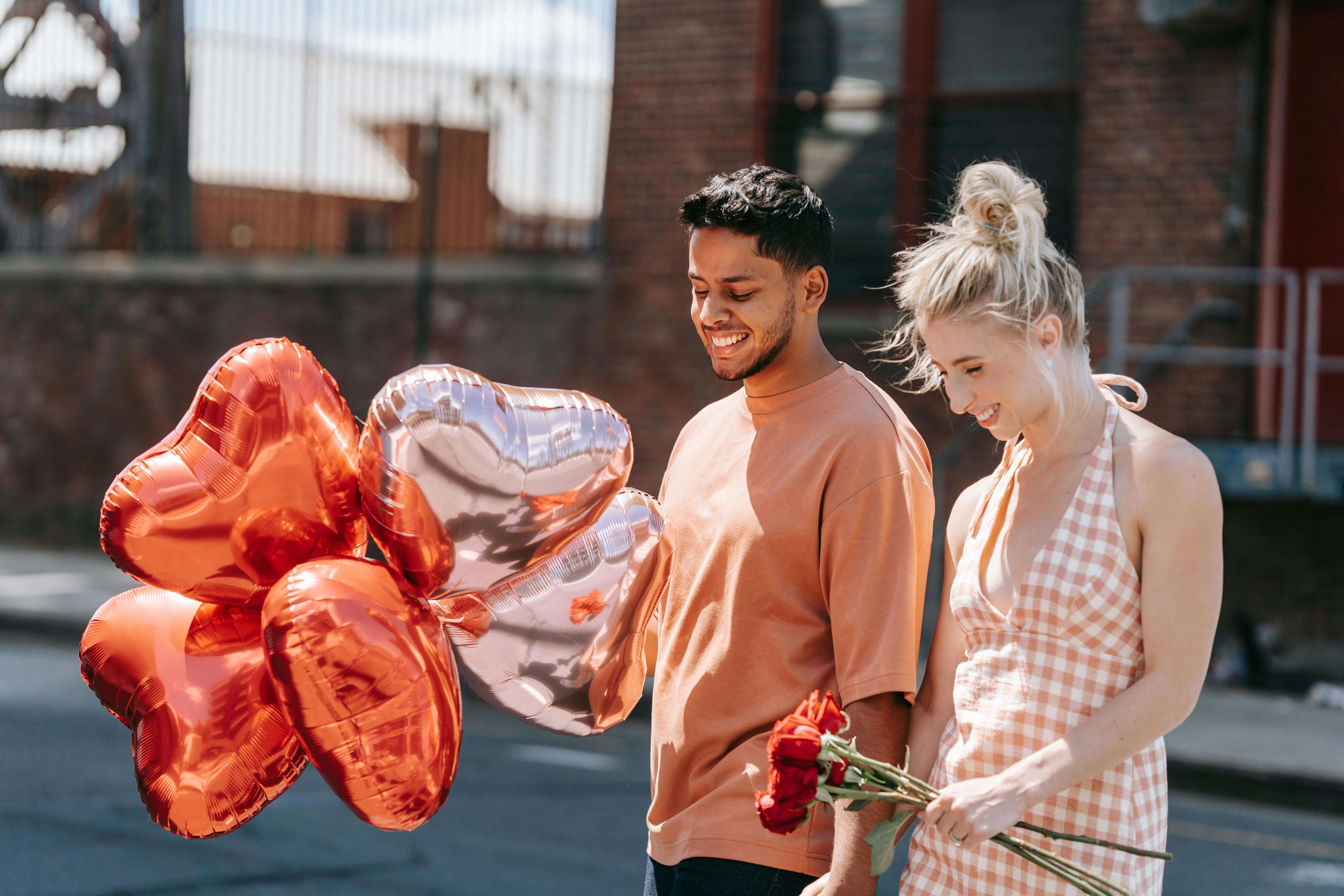 A joyful couple walks with heart-shaped balloons and roses, embodying romance.