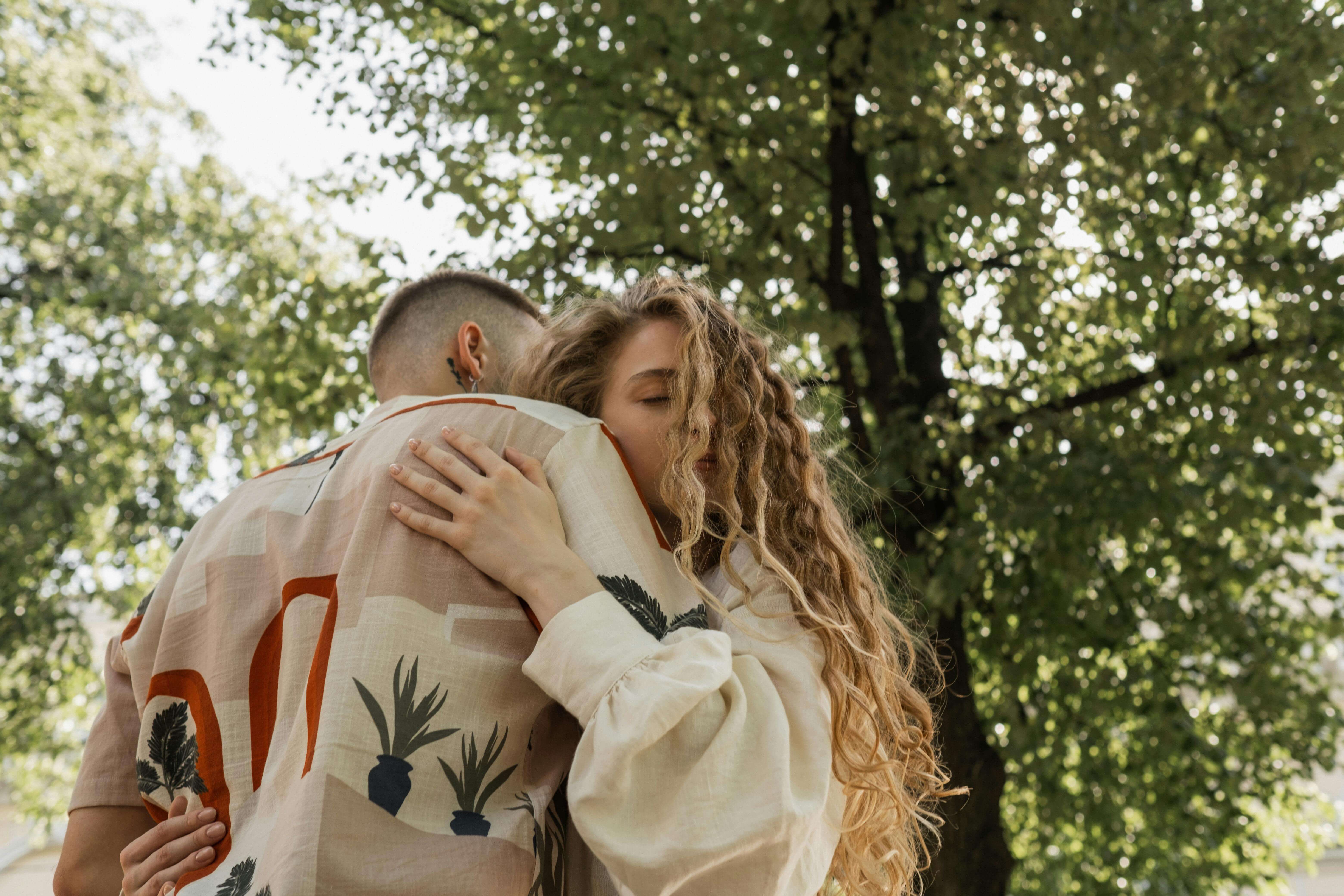 Couple embracing outdoors amidst sunlit trees, expressing love and affection.