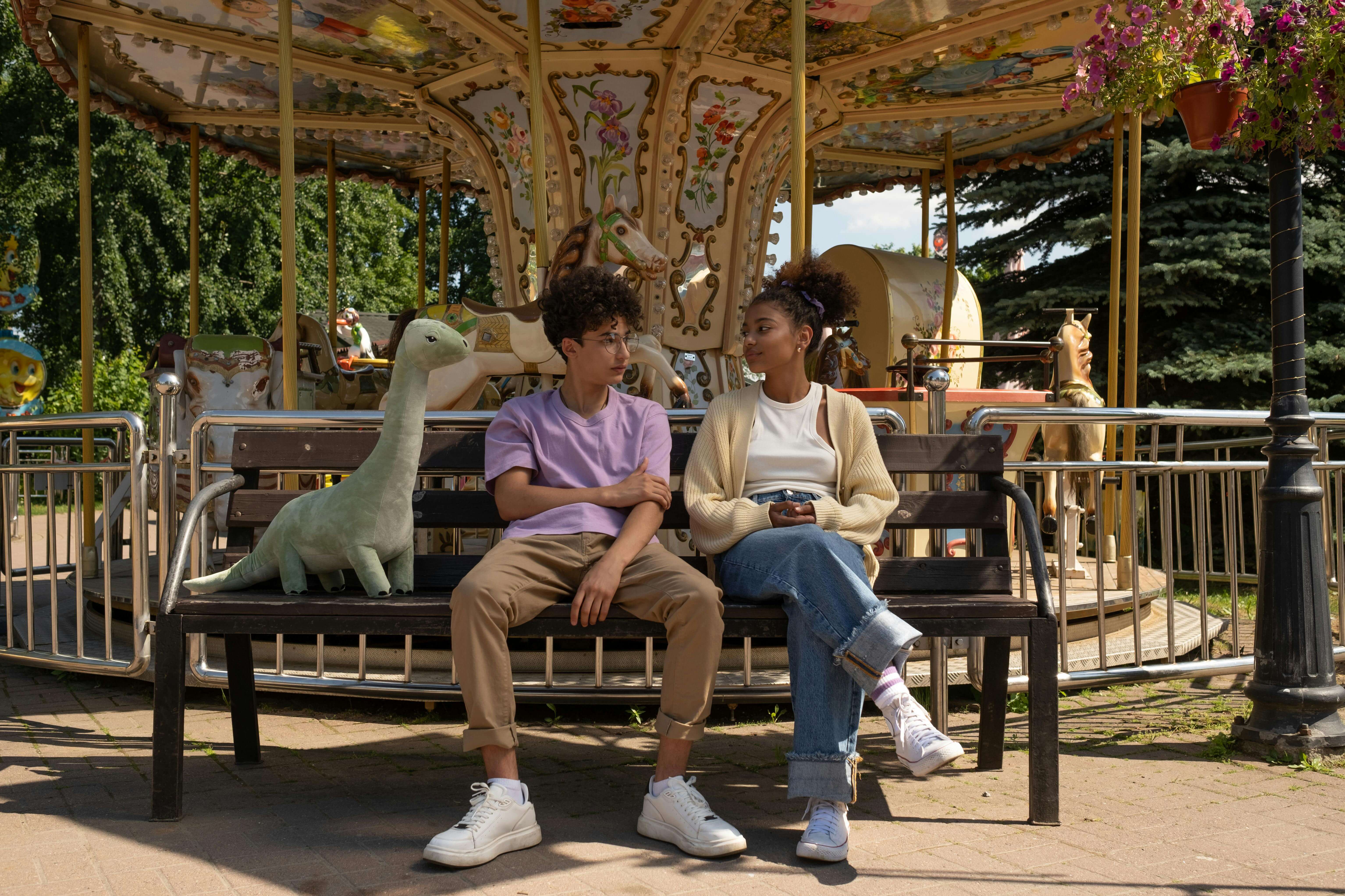 A couple enjoys a relaxing moment on a bench in front of a carousel at an amusement park.
